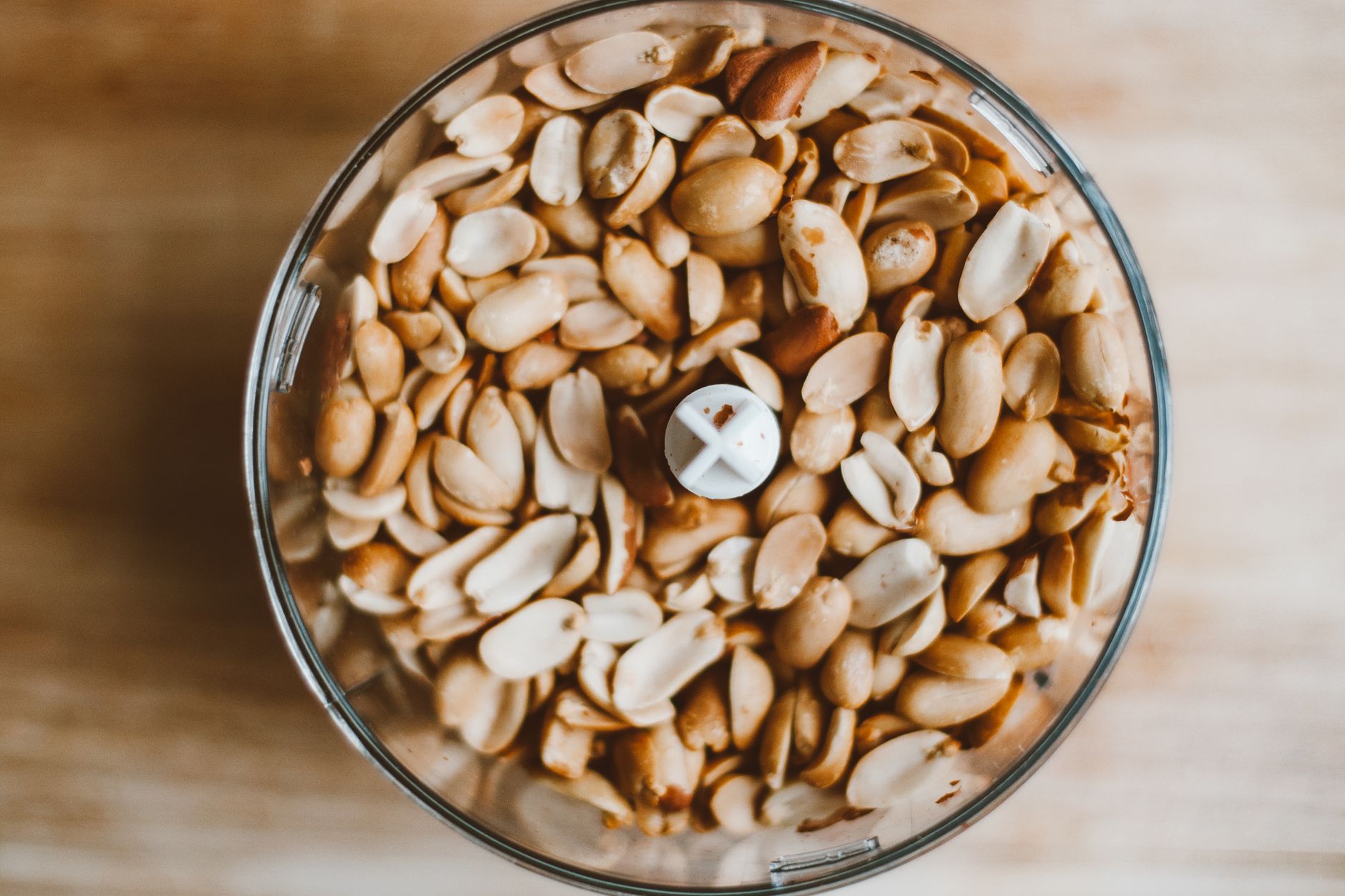 A close-up of raw shelled peanuts in a food processor viewed from above.