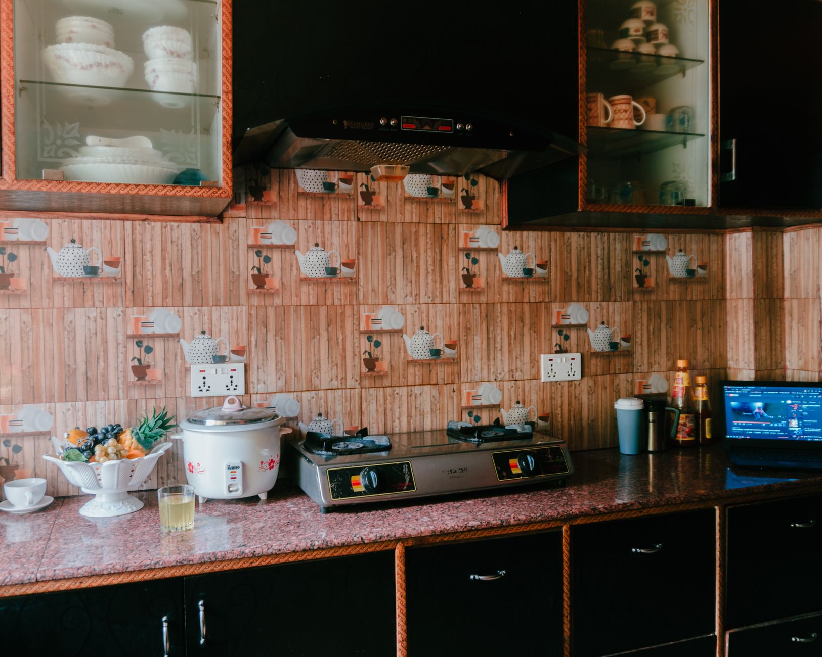 A cozy kitchen featuring a rice cooker, stove, and rustic wooden decor with glass cabinets.