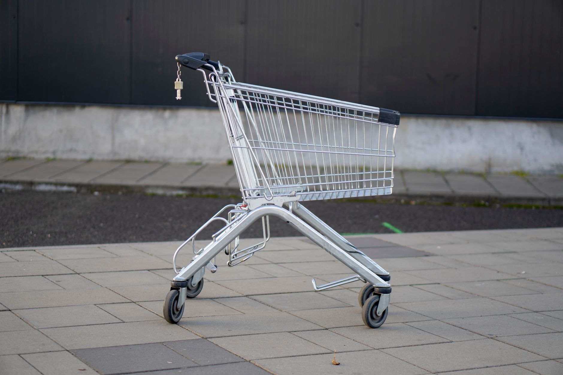 A lone metal shopping cart on an empty pavement outside a store.