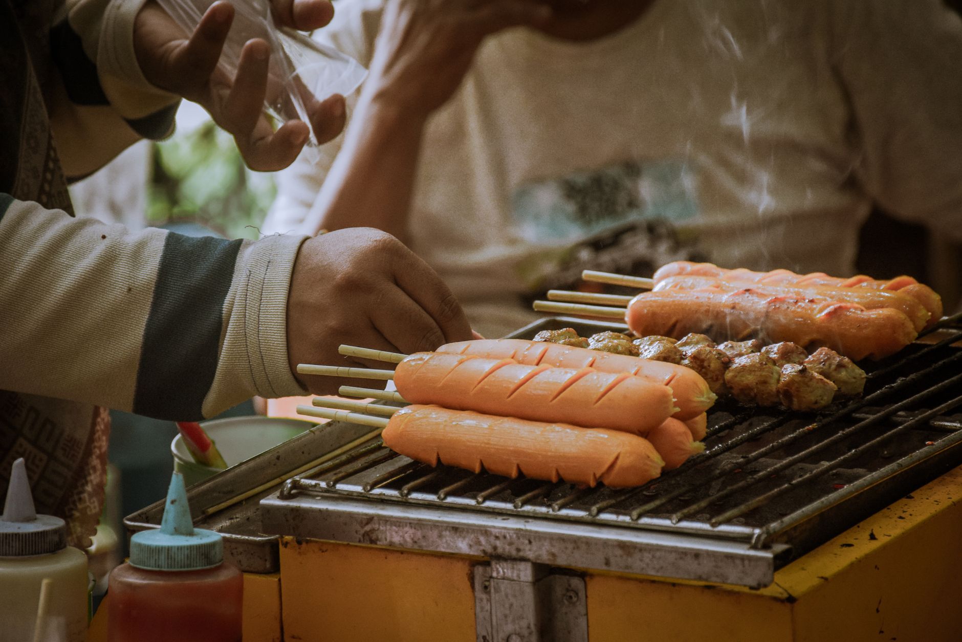 Close-up of a vendor grilling skewered sausages on a street food stall, perfect for culinary and cultural themes.