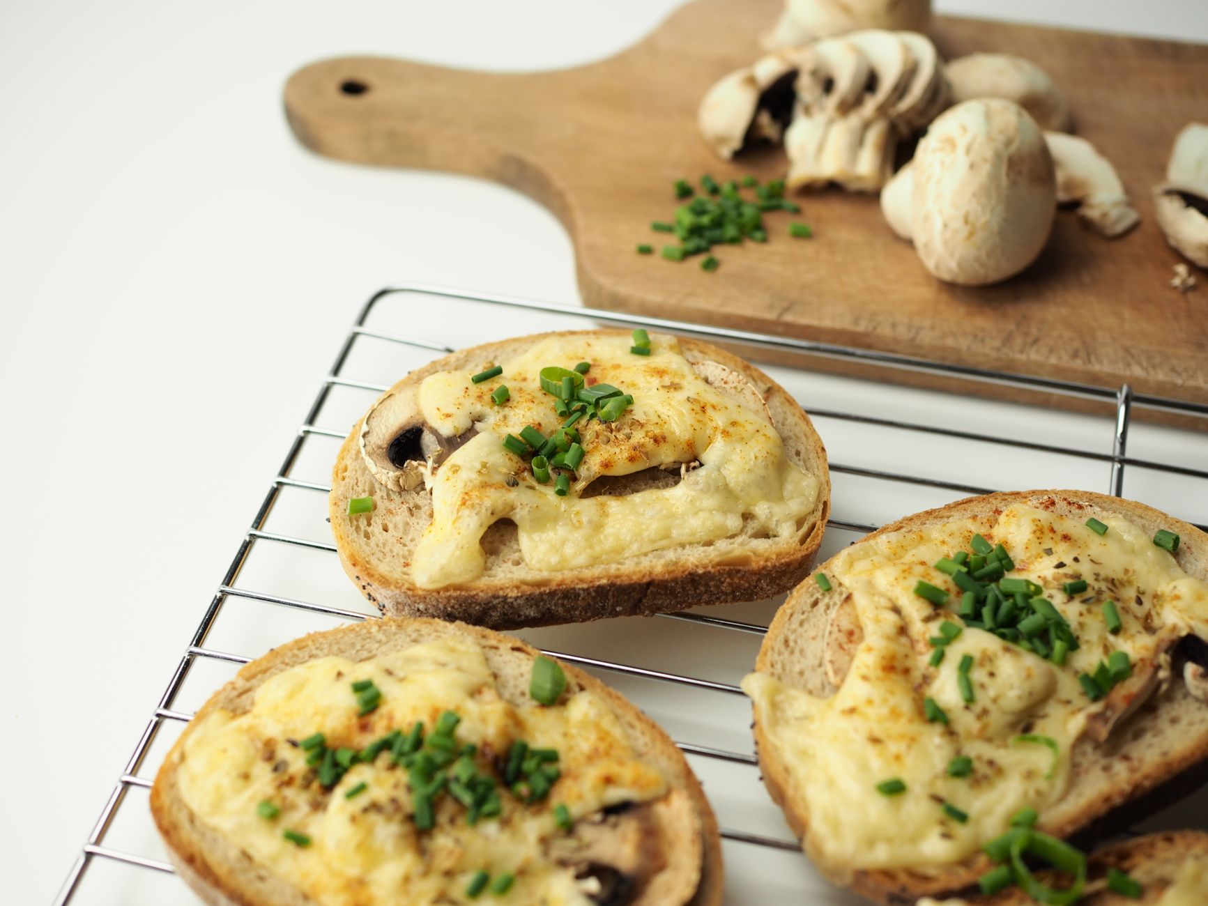 Delicious cheesy bread toast topped with mushrooms and fresh chives, perfect for breakfast.