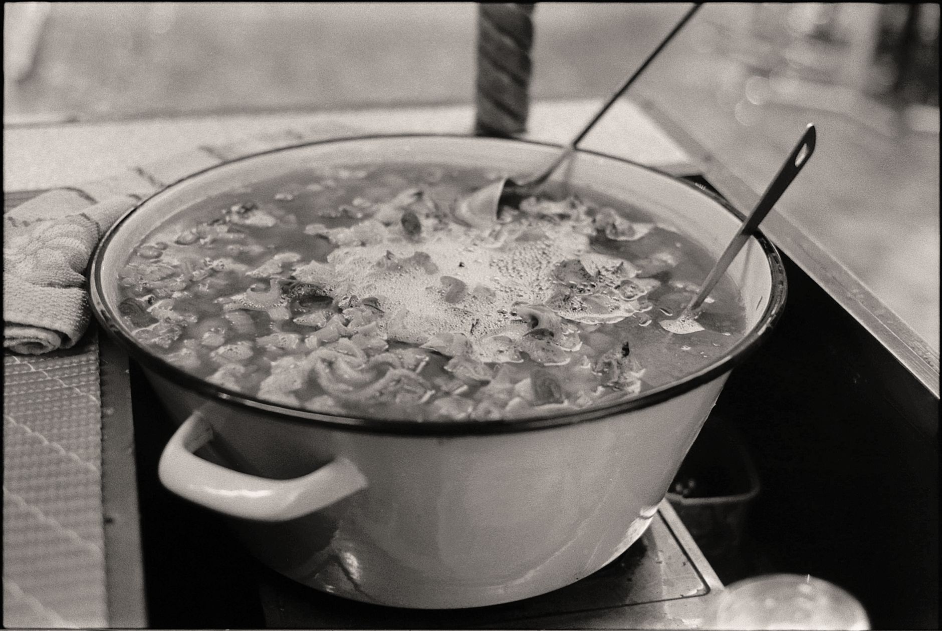 A vintage style black and white photo of a steaming pot of soup, depicting rustic cooking.