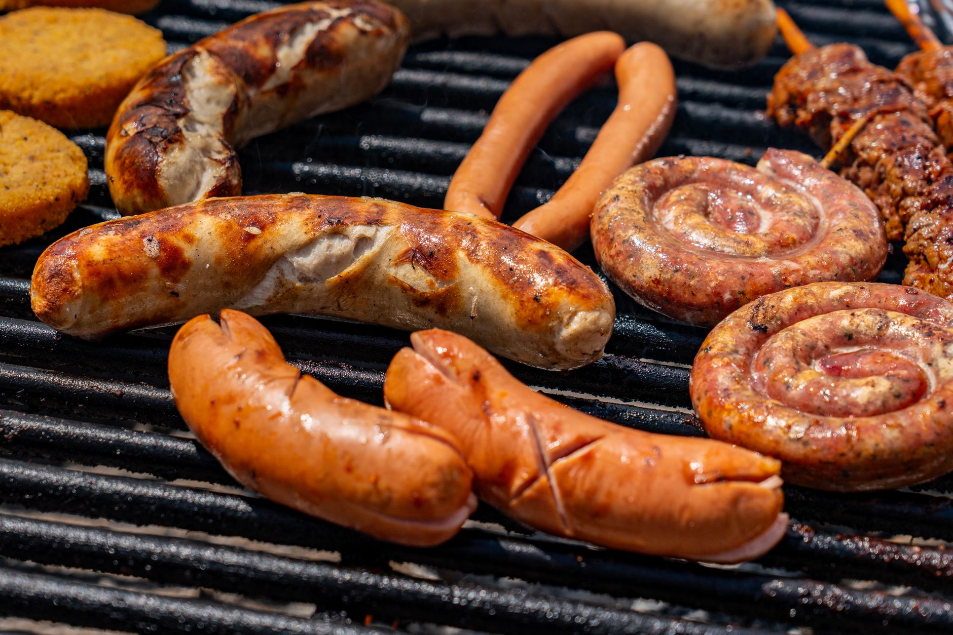 A variety of sausages and meats grilling on an outdoor barbecue grill, perfect for summer cookouts.