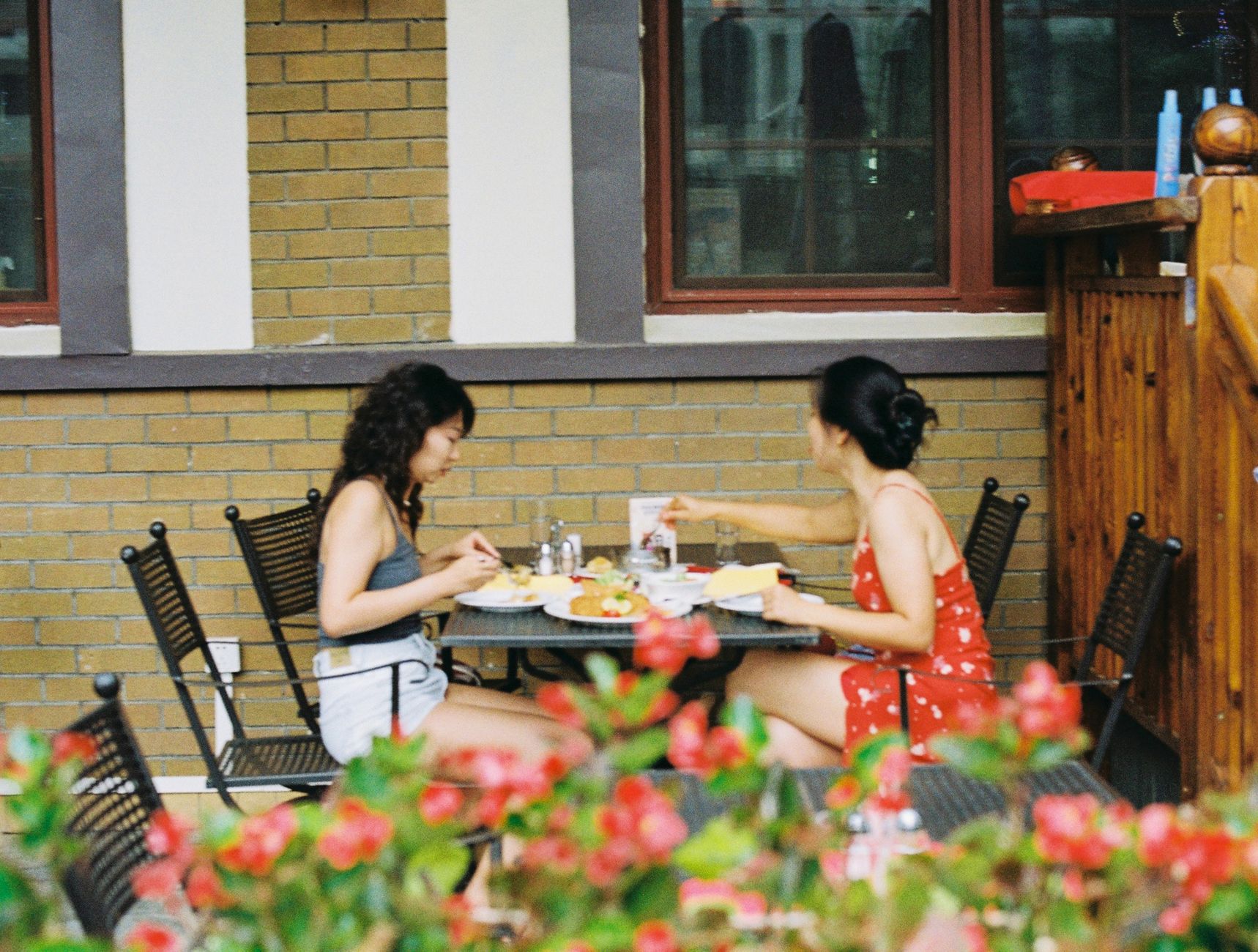 Two women enjoying a meal outdoors in a bright, summery setting.