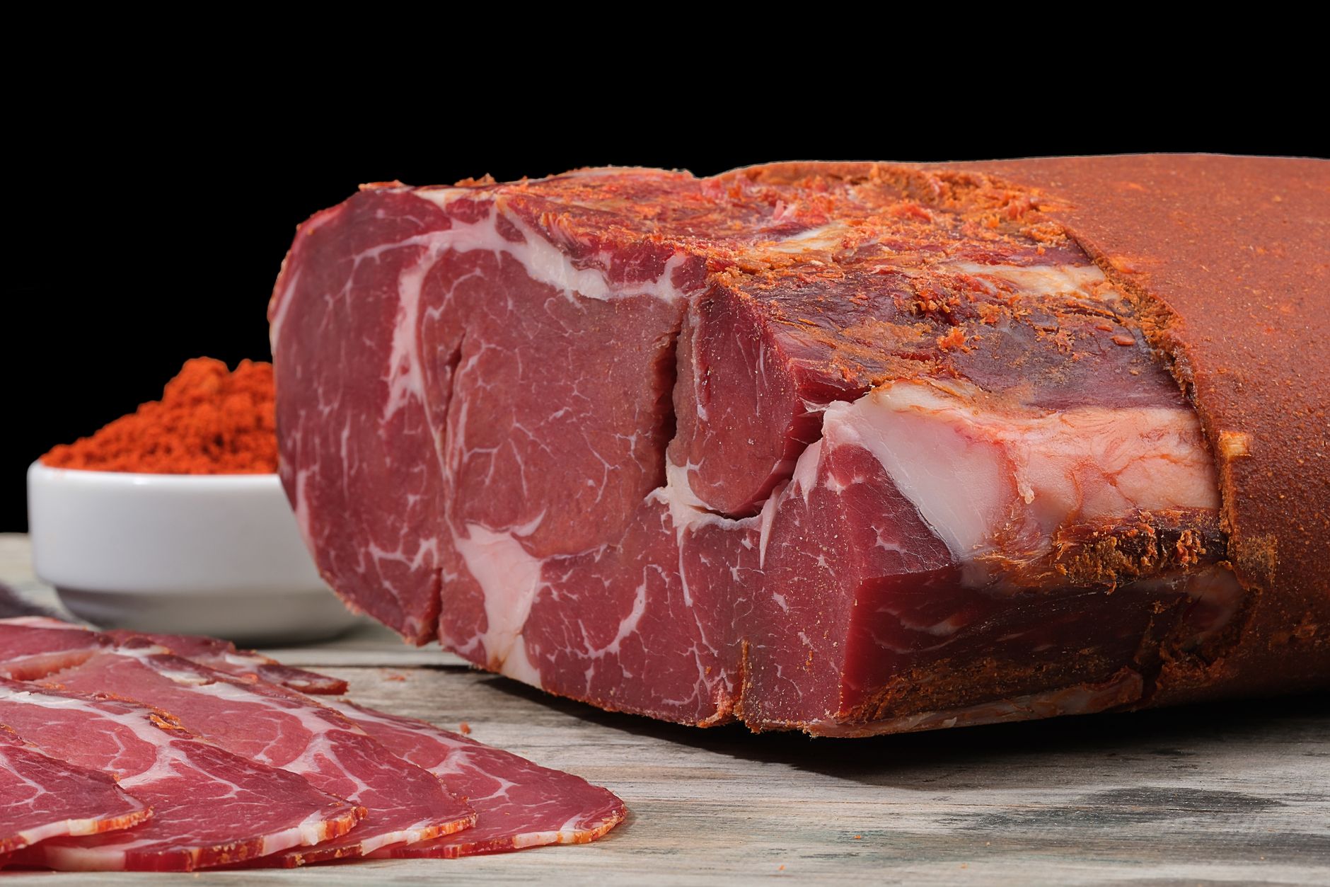 Close-up of cured beef with paprika on a rustic wooden surface, highlighting vibrant textures.