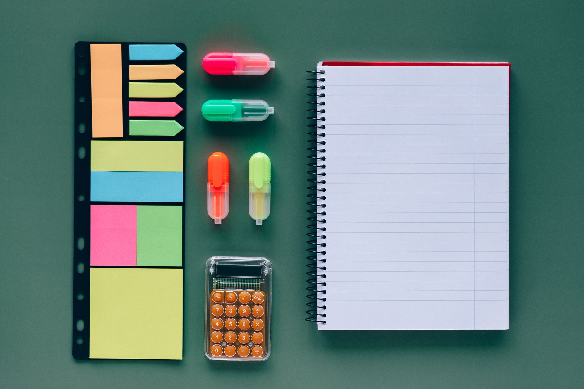 Top view of vibrant office supplies on a green background, including notebook and calculator.