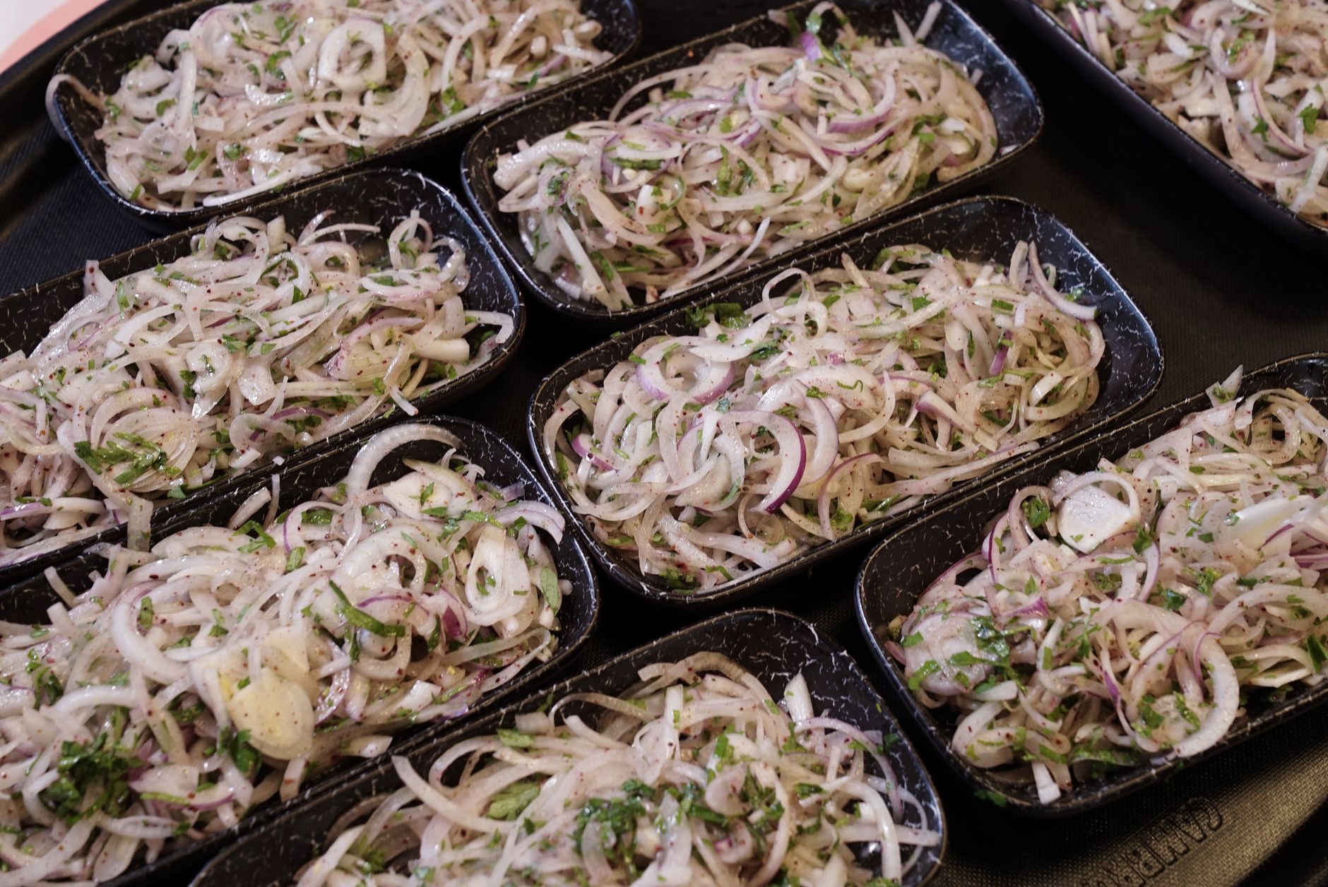 Rows of sliced onion salads garnished with herbs in black serving plates.