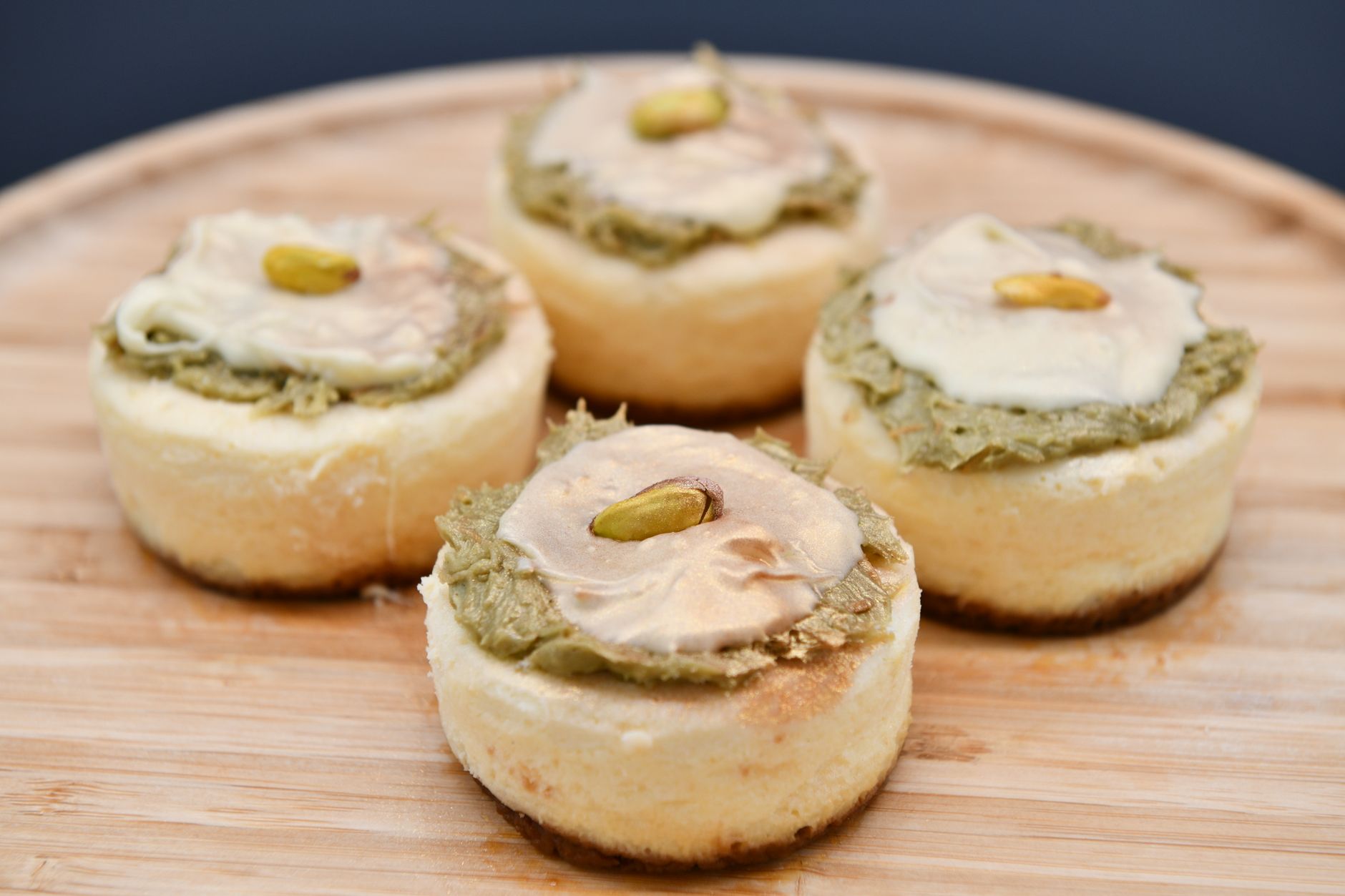 Delicious mini cheesecakes topped with pistachio cream on a wooden board.