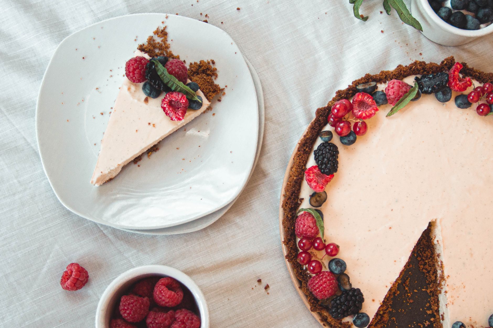 Flatlay of a berry cheesecake with a slice on a white plate, featuring fresh berries and a crumbly base.