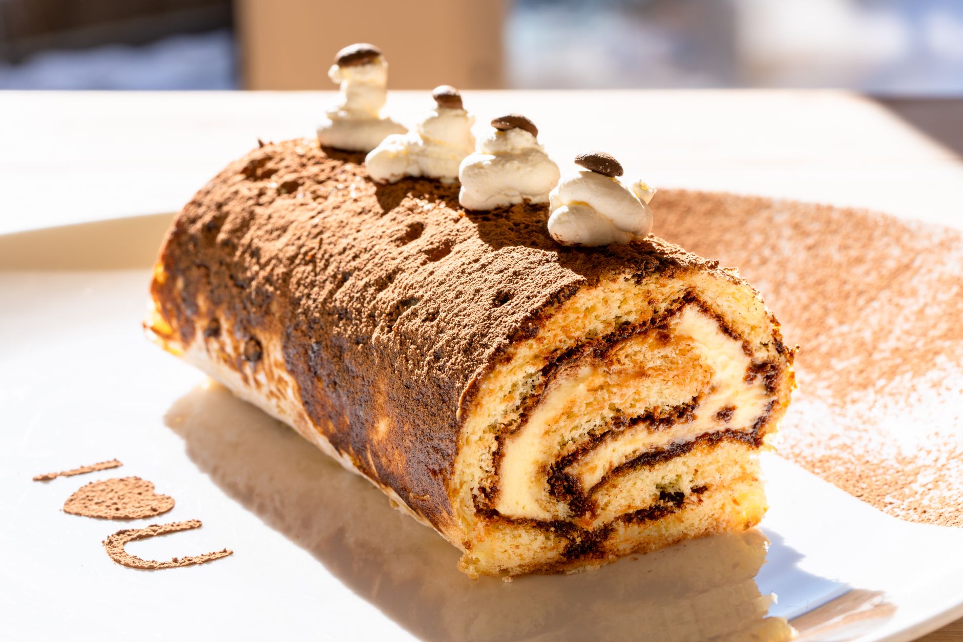 Closeup of a homemade tiramisu Swiss roll with cream and cocoa topping.