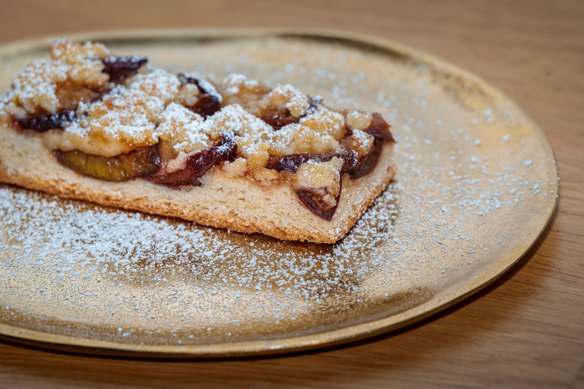Plum tart with a crumble topping on a golden plate, dusted with powdered sugar.
