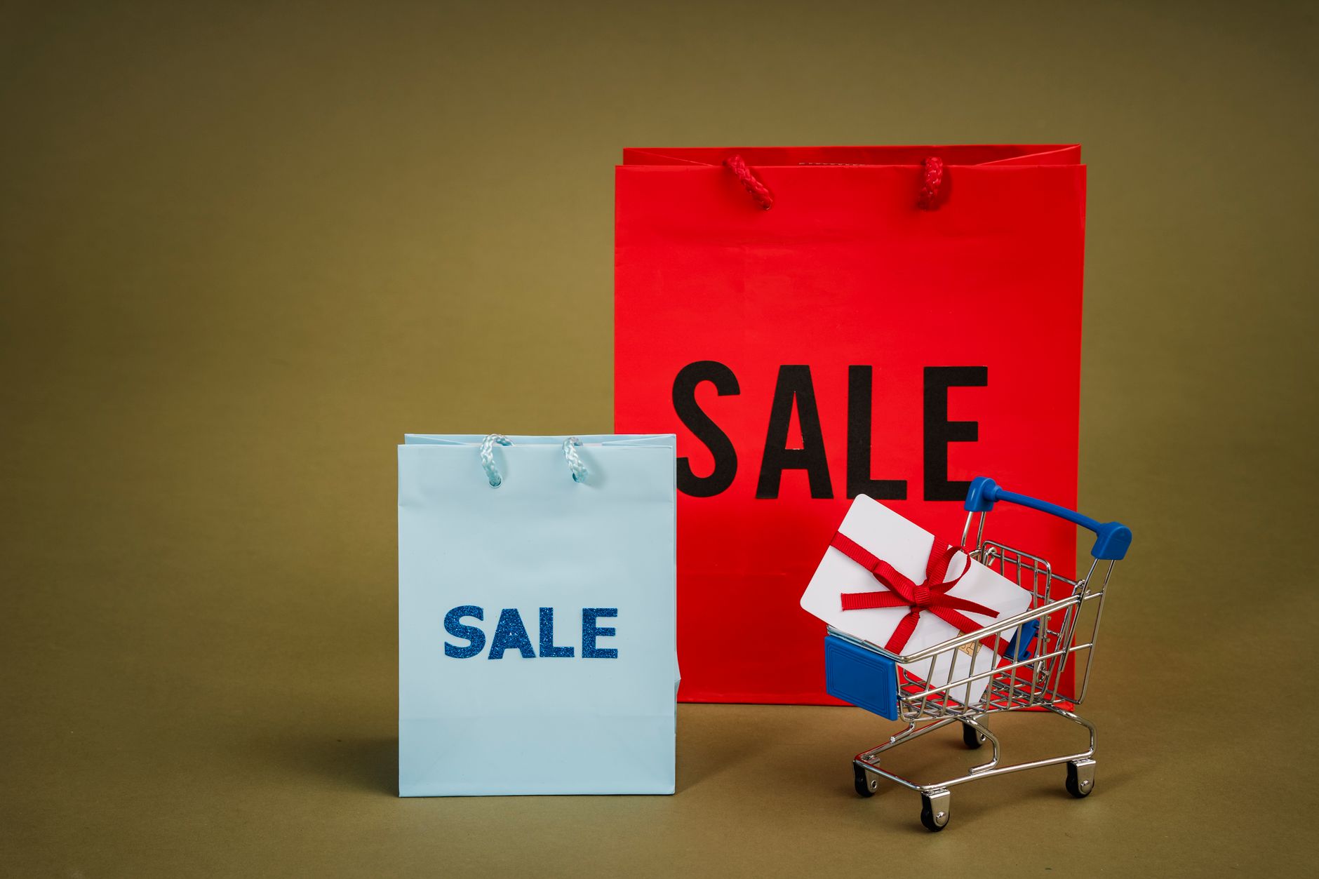 Bright sale bags with a gift in a shopping cart against a neutral background.
