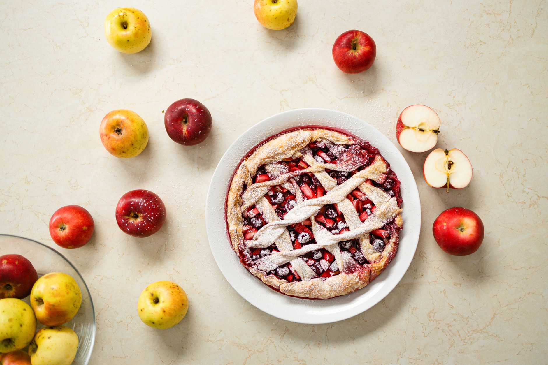 Delicious homemade apple pie with lattice crust surrounded by fresh apples on a marble surface.