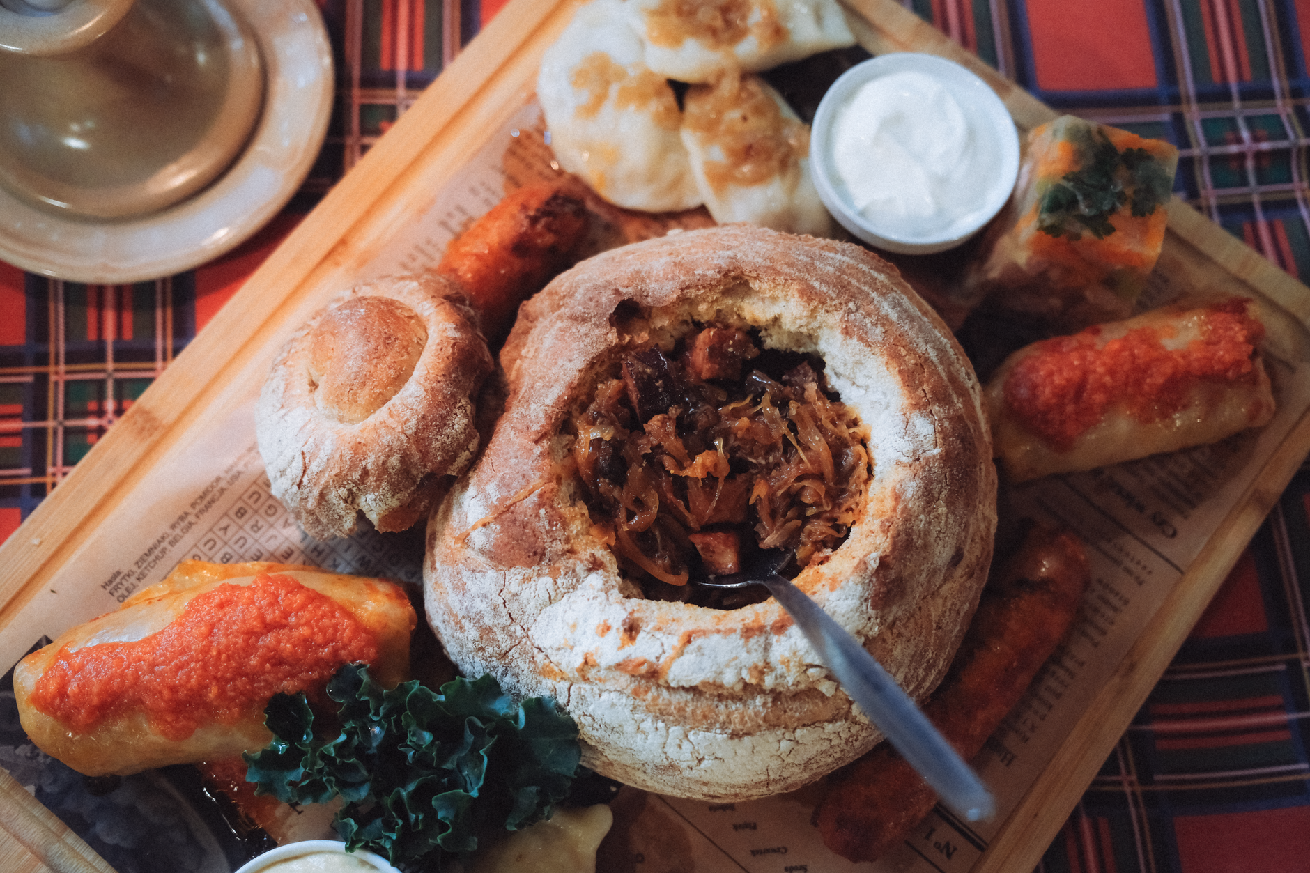 Delicious traditional Polish meal served in a bread bowl, with assorted side dishes on a wooden platter.