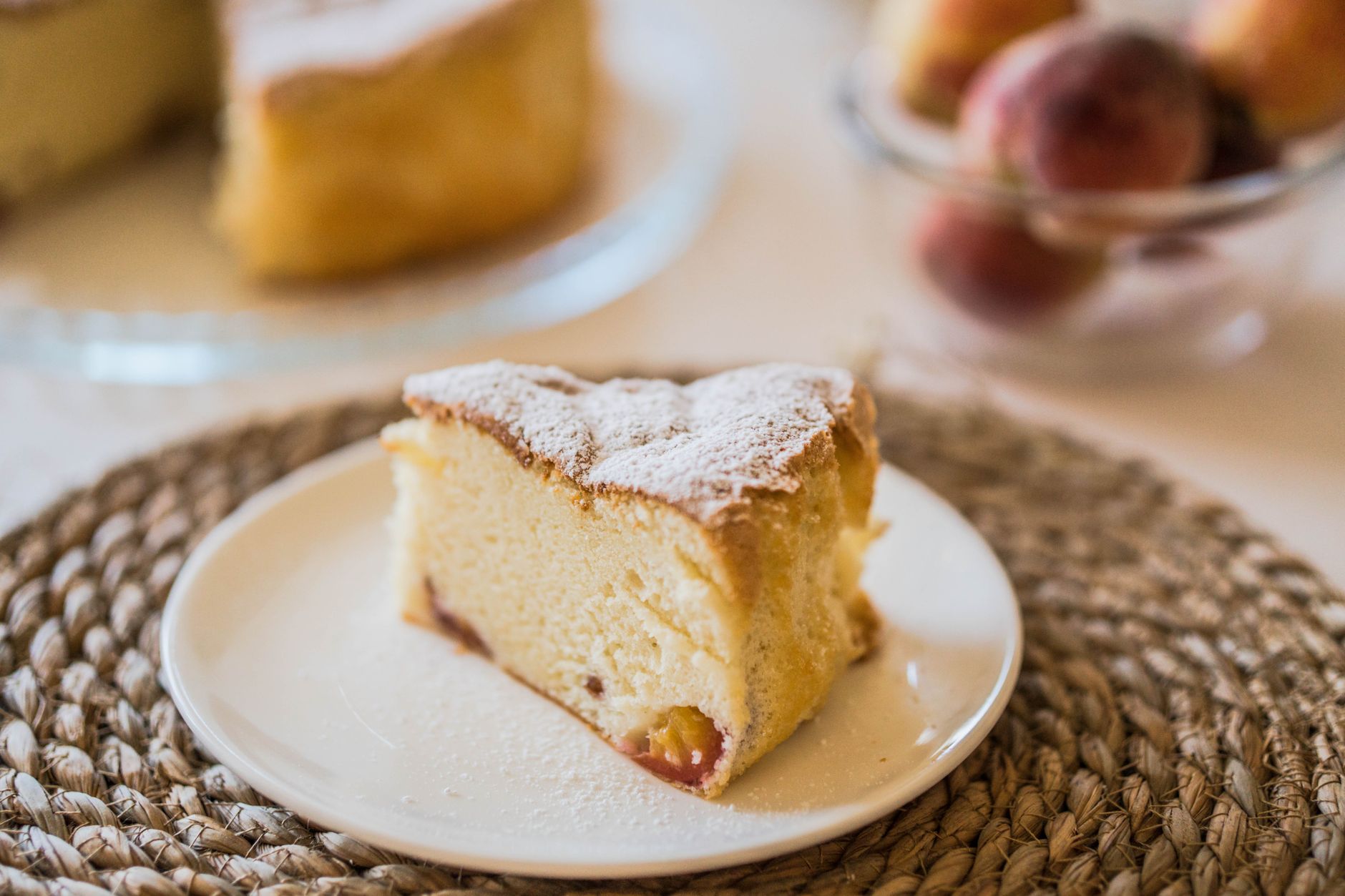 A slice of fluffy peach cake with powdered sugar on a white plate, perfect for dessert lovers.