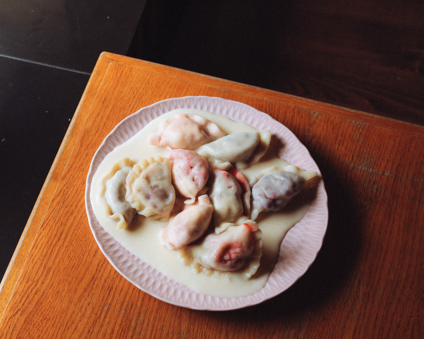 A plate of colorful Polish pierogi dumplings served in a creamy sauce on a wooden table.