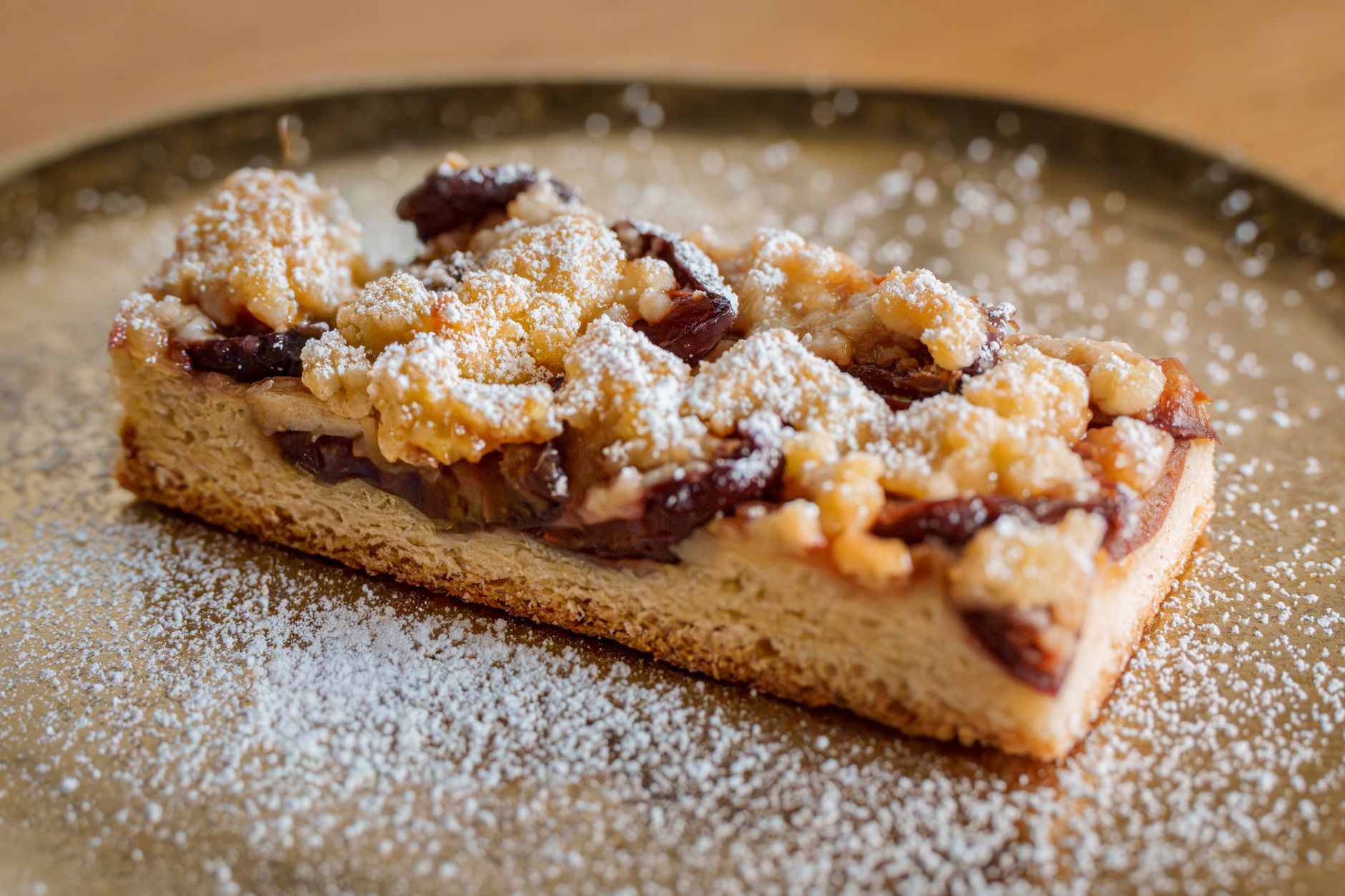Slice of plum crumble cake on a plate dusted with powdered sugar.