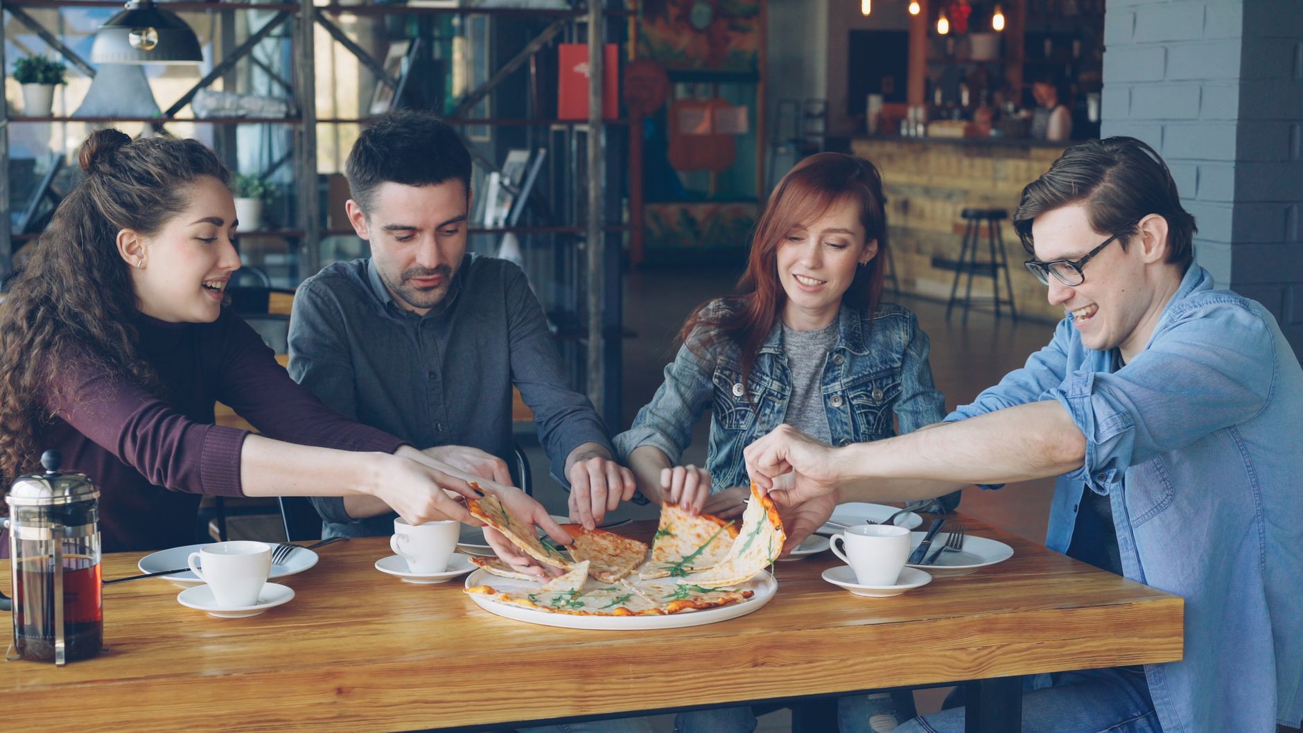 A group of friends enjoying pizza and coffee in a casual café setting.