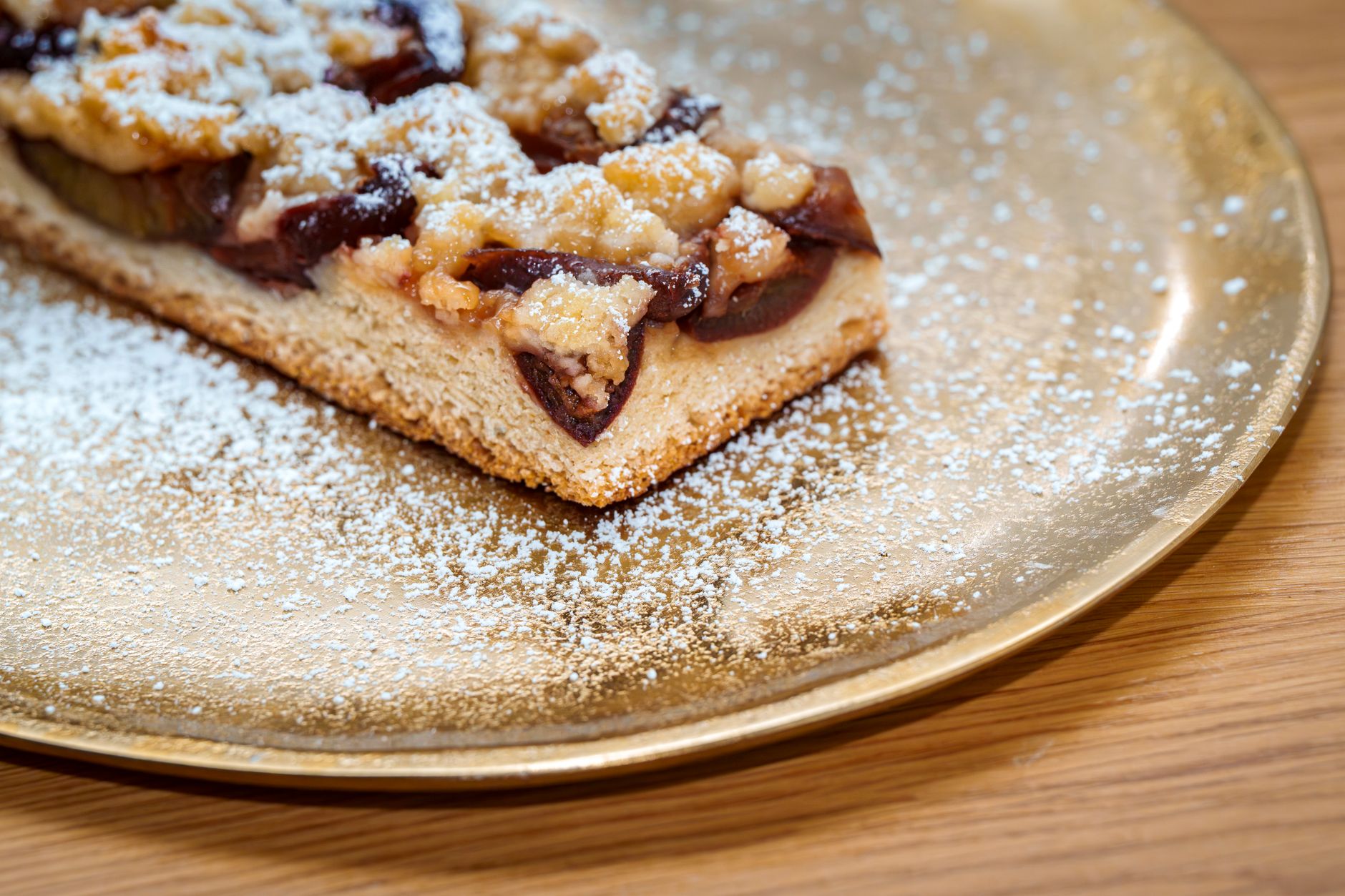 A close-up of a delicious plum tart dusted with powdered sugar, served on a golden plate.