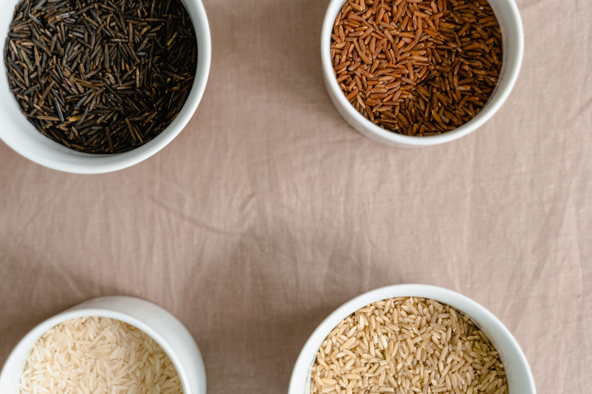 Top view of four ceramic bowls filled with different types of rice on a neutral background.