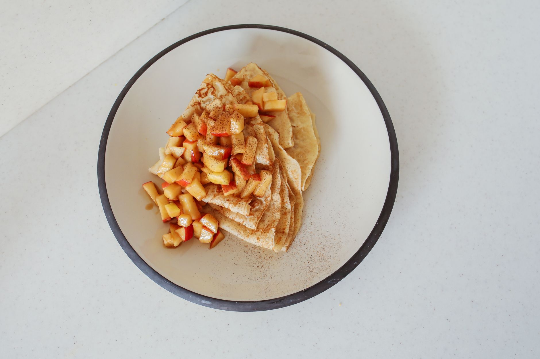 Tasty crepes topped with apple cinnamon served on a plate, photographed from above.
