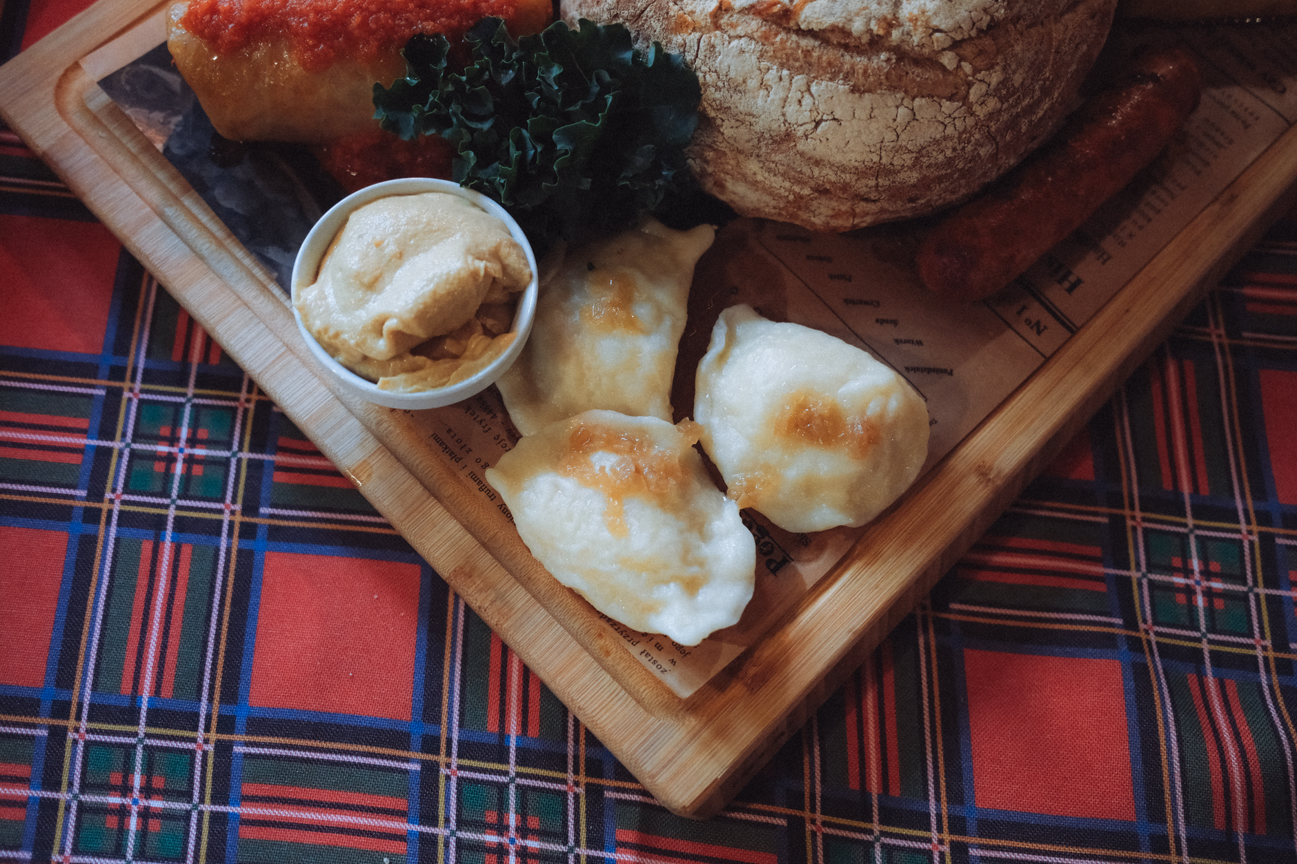 A wooden board with Polish pierogi, bread, and sausages on plaid tablecloth, showcasing authentic Polish cuisine.