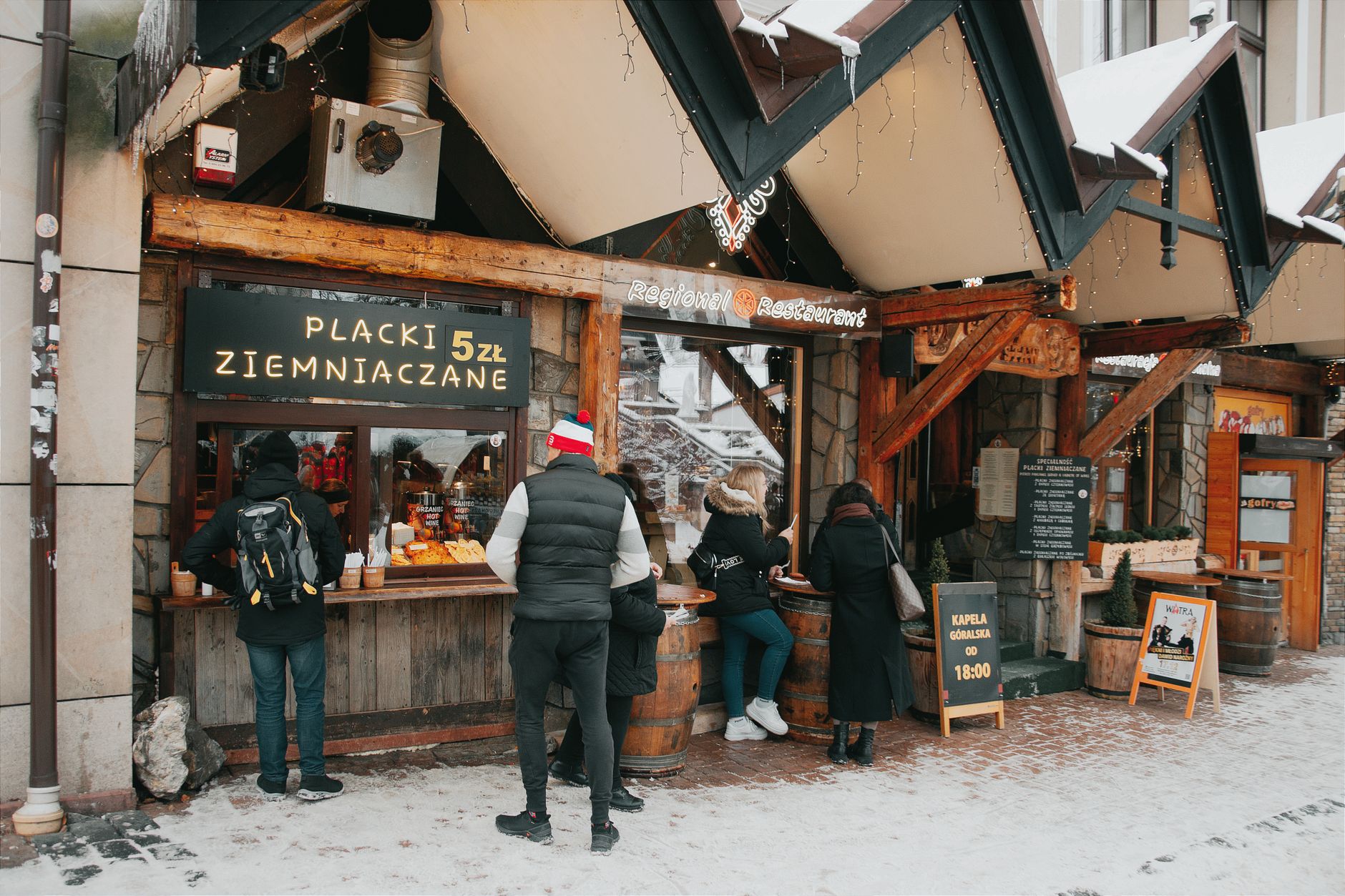People buying traditional Polish potato cakes at a street stall in snowy Zakopane.