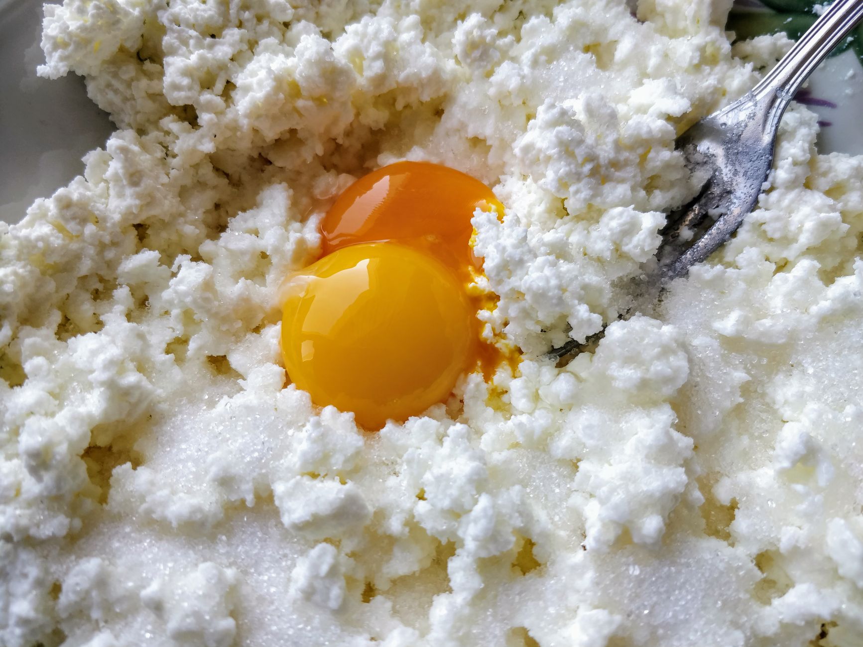 A close-up view of fresh ricotta cheese mixed with raw egg yolks, ready for cooking.