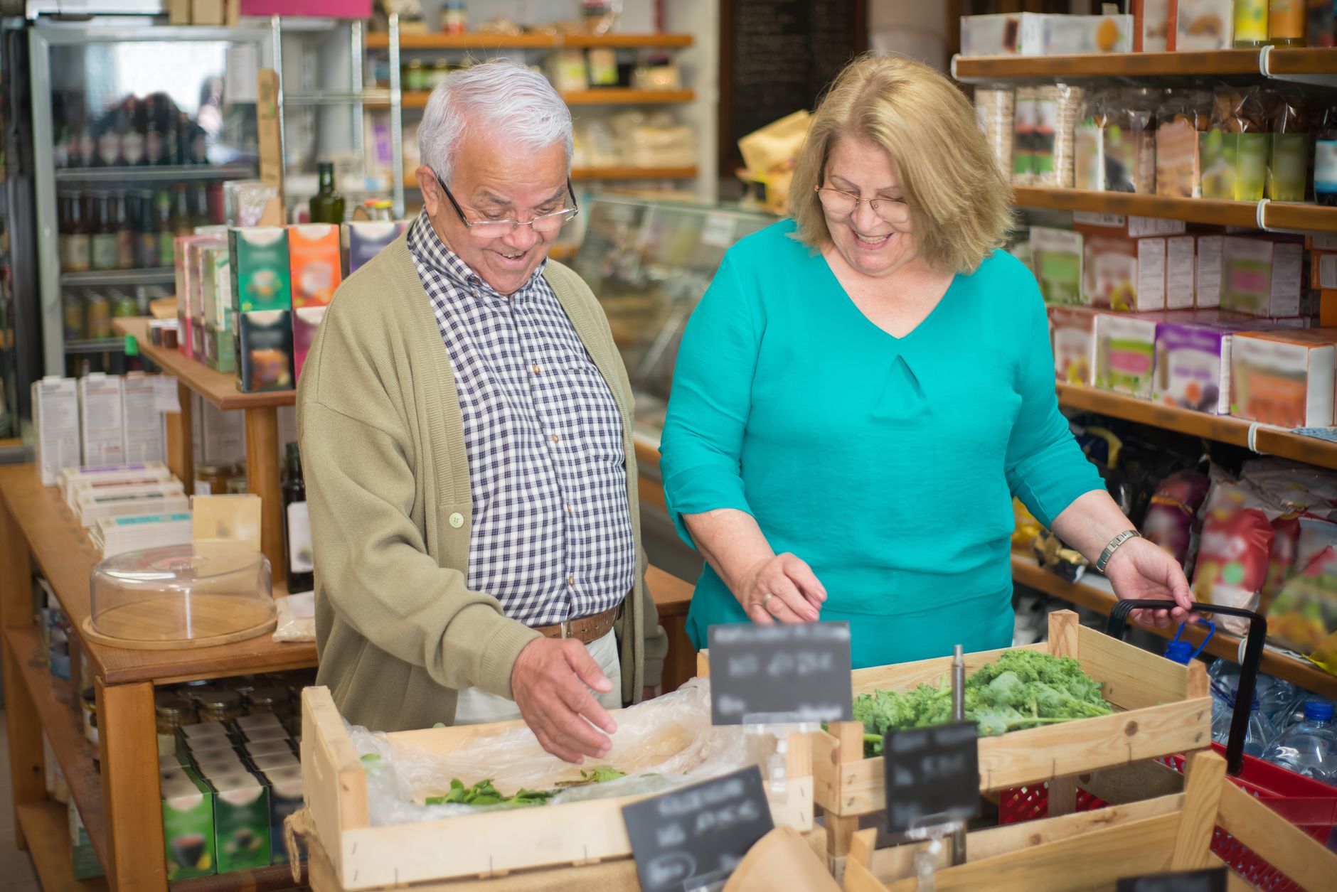 Smiling elderly couple grocery shopping, selecting fresh produce in a Portuguese store.