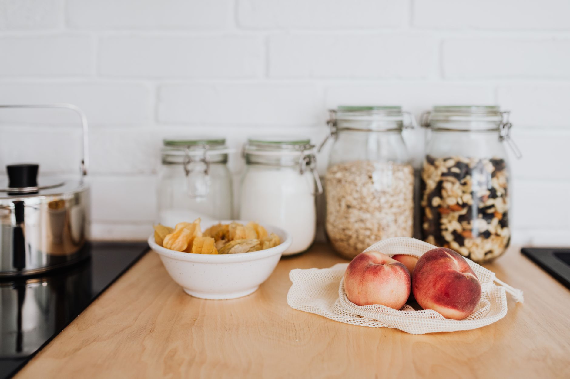A selection of zero waste kitchen essentials with reusable jars and fresh fruit on a wooden countertop.