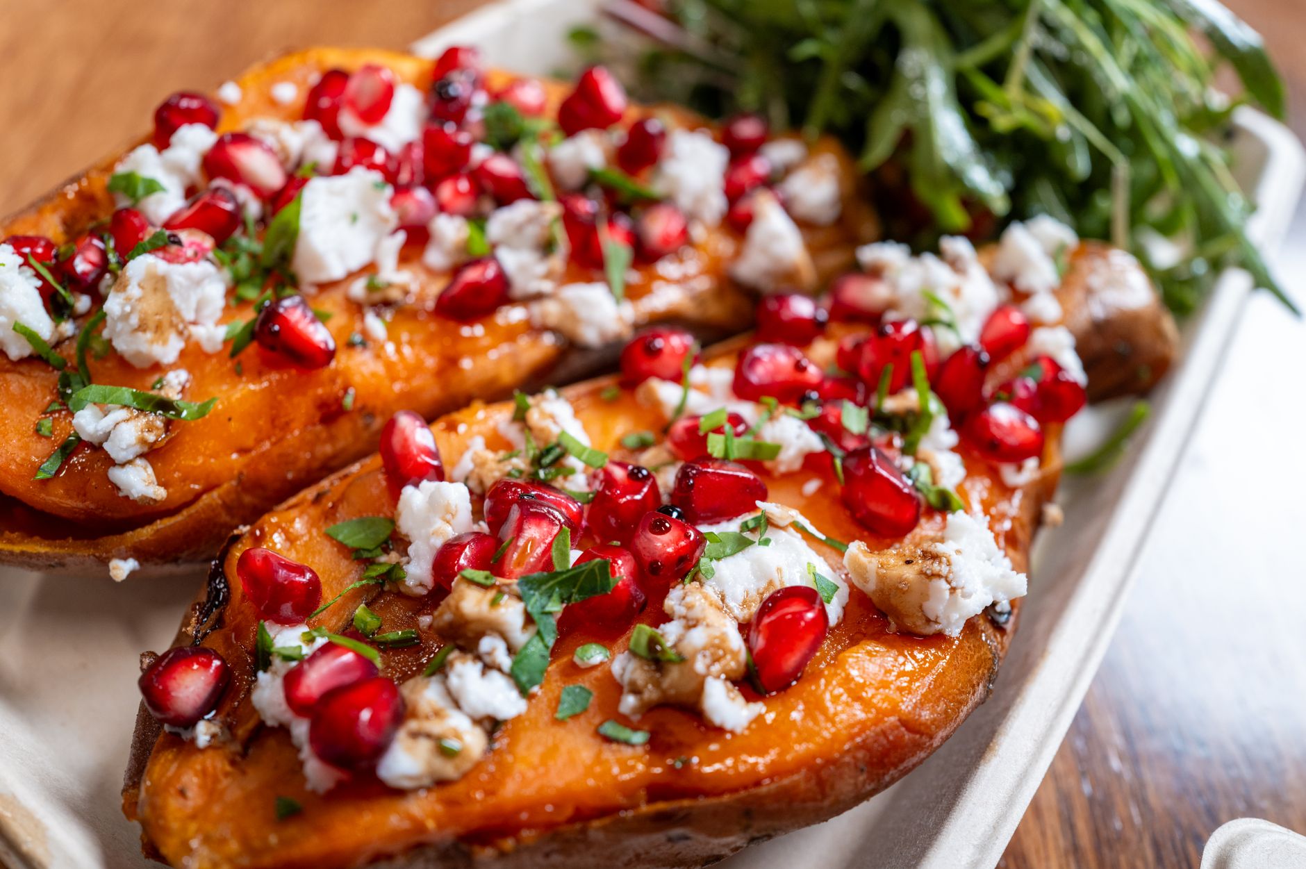 Stuffed sweet potatoes topped with feta cheese, pomegranate, herbs, and served with fresh greens.