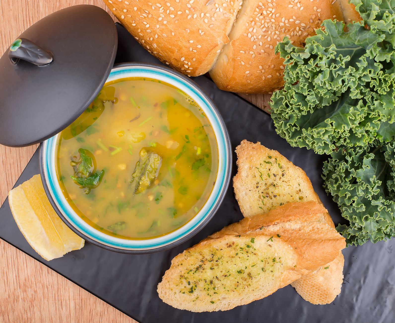 Delicious soup served with garlic bread, kale, and fresh loaf on a table.