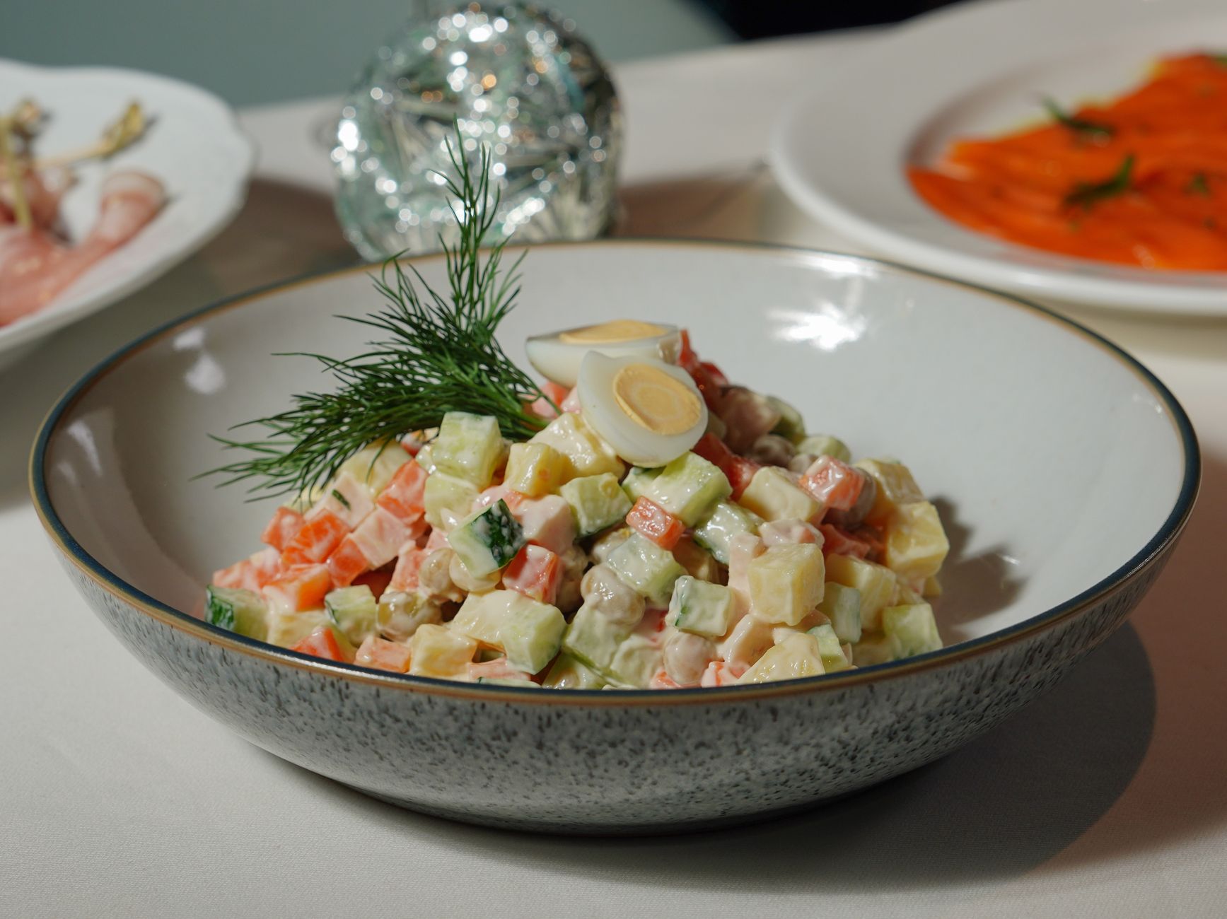 Colorful vegetable salad garnished with dill and quail eggs in a speckled ceramic bowl.