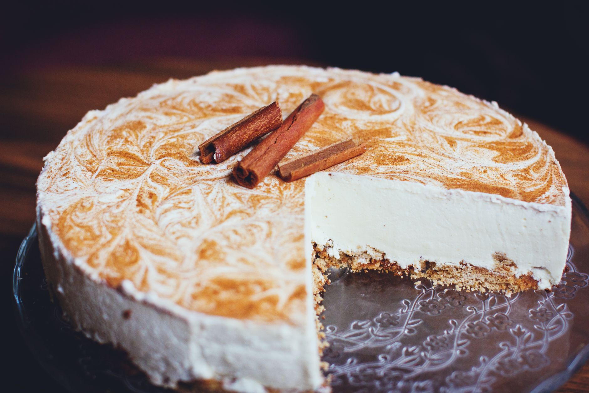 Delicious cinnamon cheesecake beautifully presented with a slice removed on a glass plate.