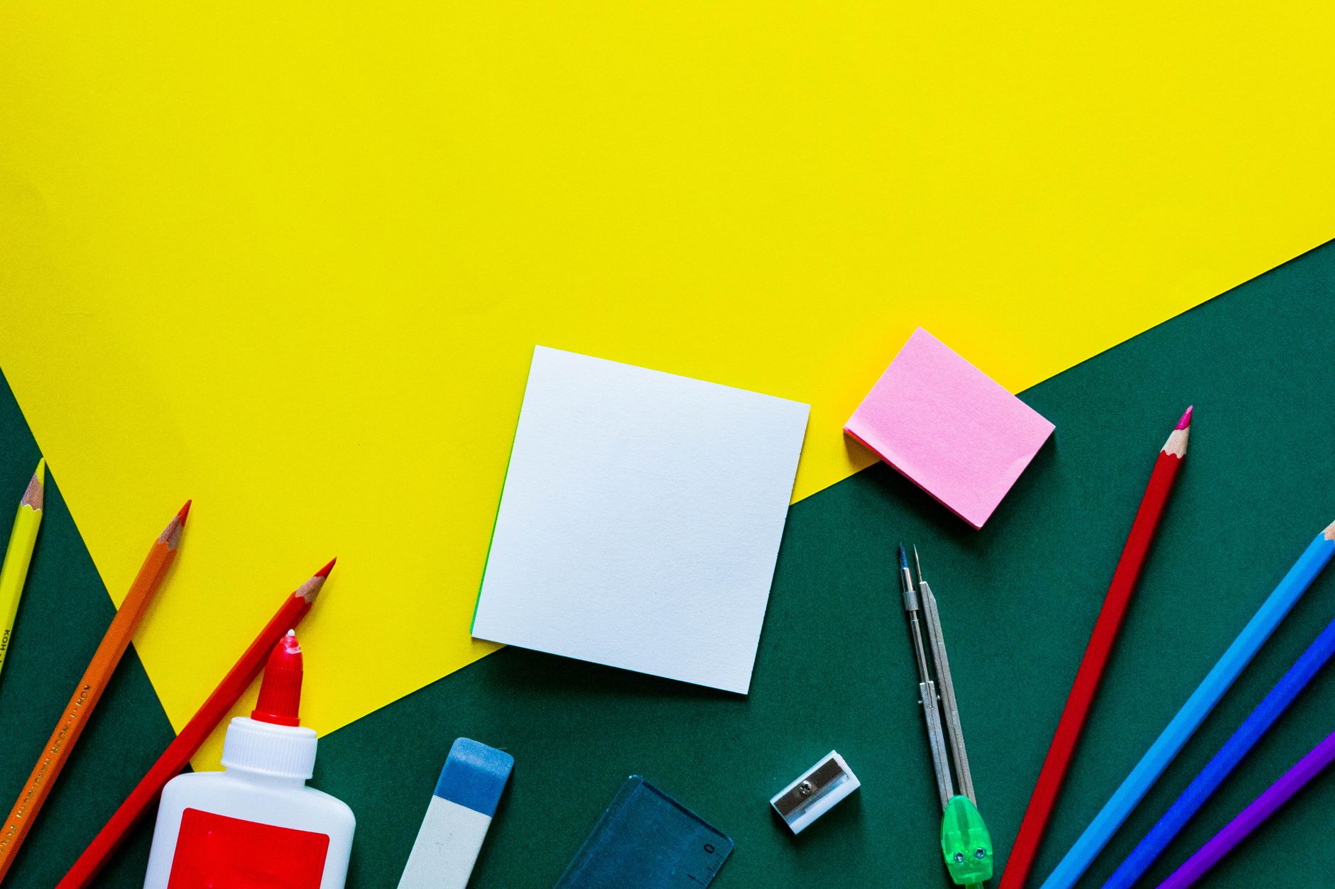 A vibrant flat lay of various school supplies on a yellow and green geometric background.