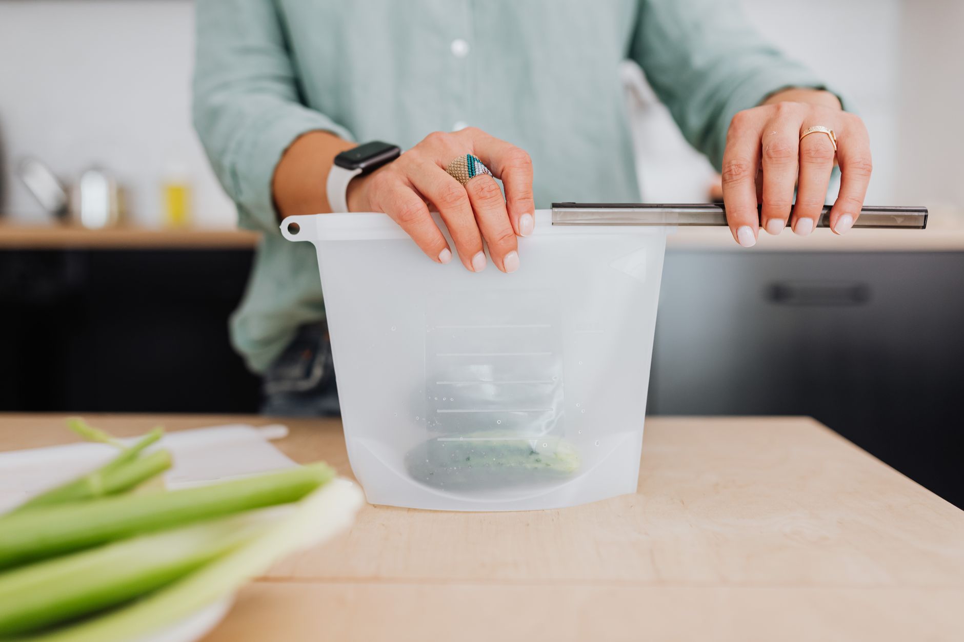 Woman sealing a reusable silicone storage pouch in a kitchen setting.
