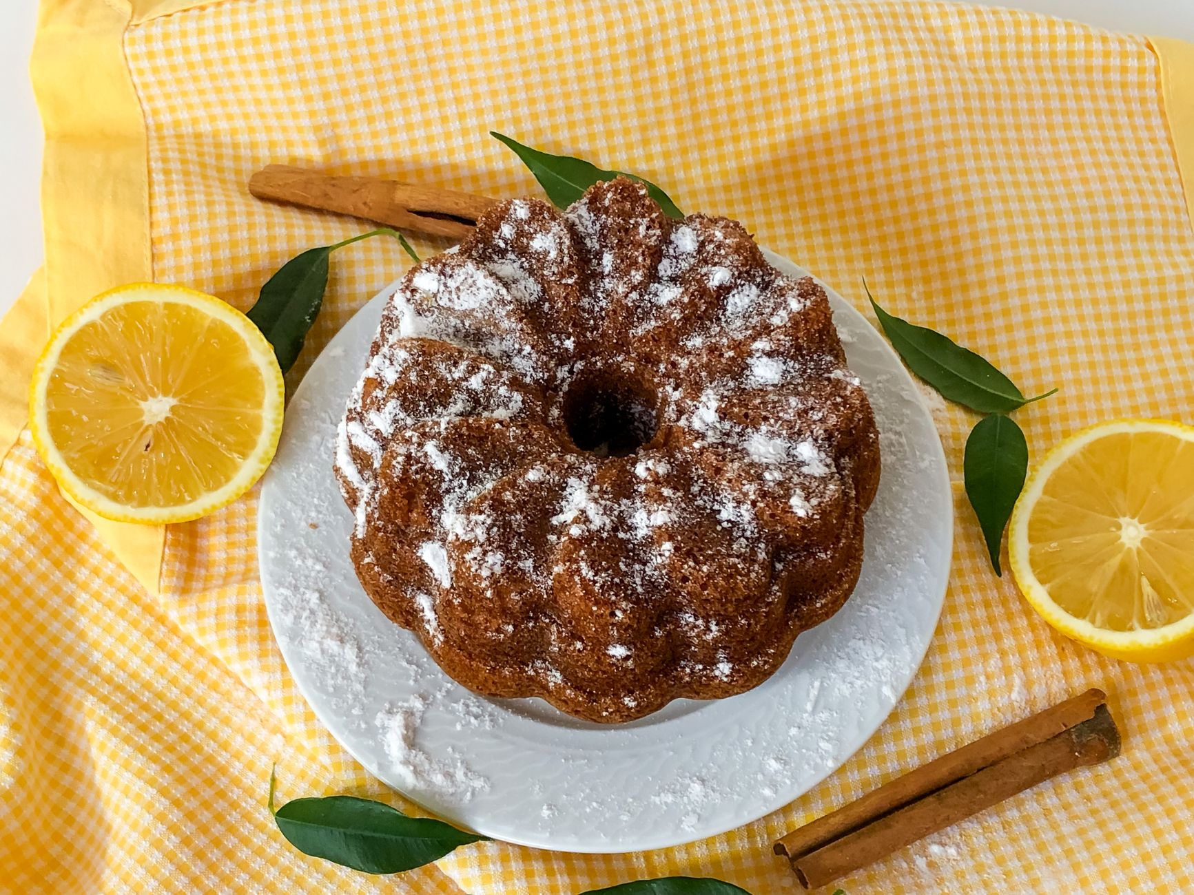 A homemade lemon bundt cake dusted with sugar on a gingham cloth.