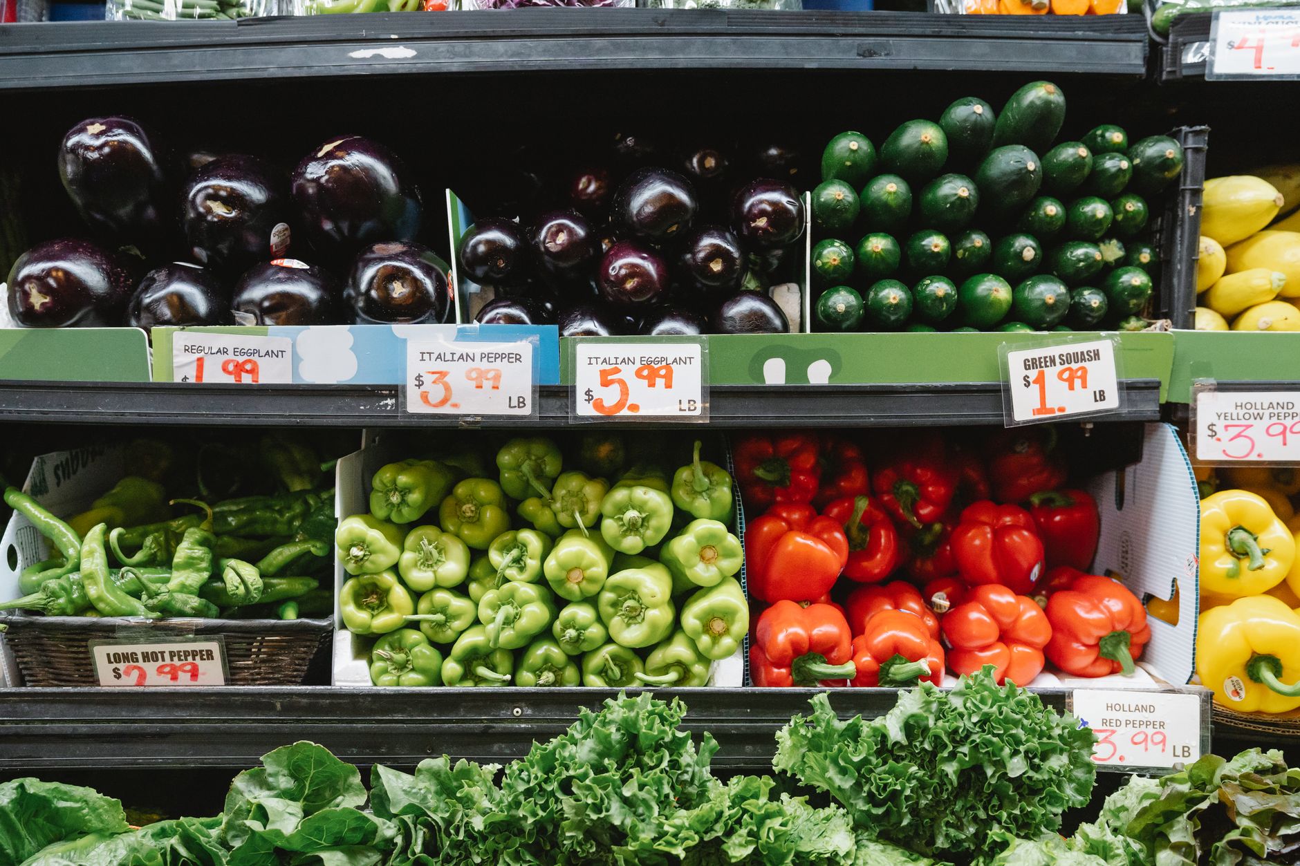 Colorful assortment of vegetables on display in a supermarket, featuring peppers, eggplants, and squash.