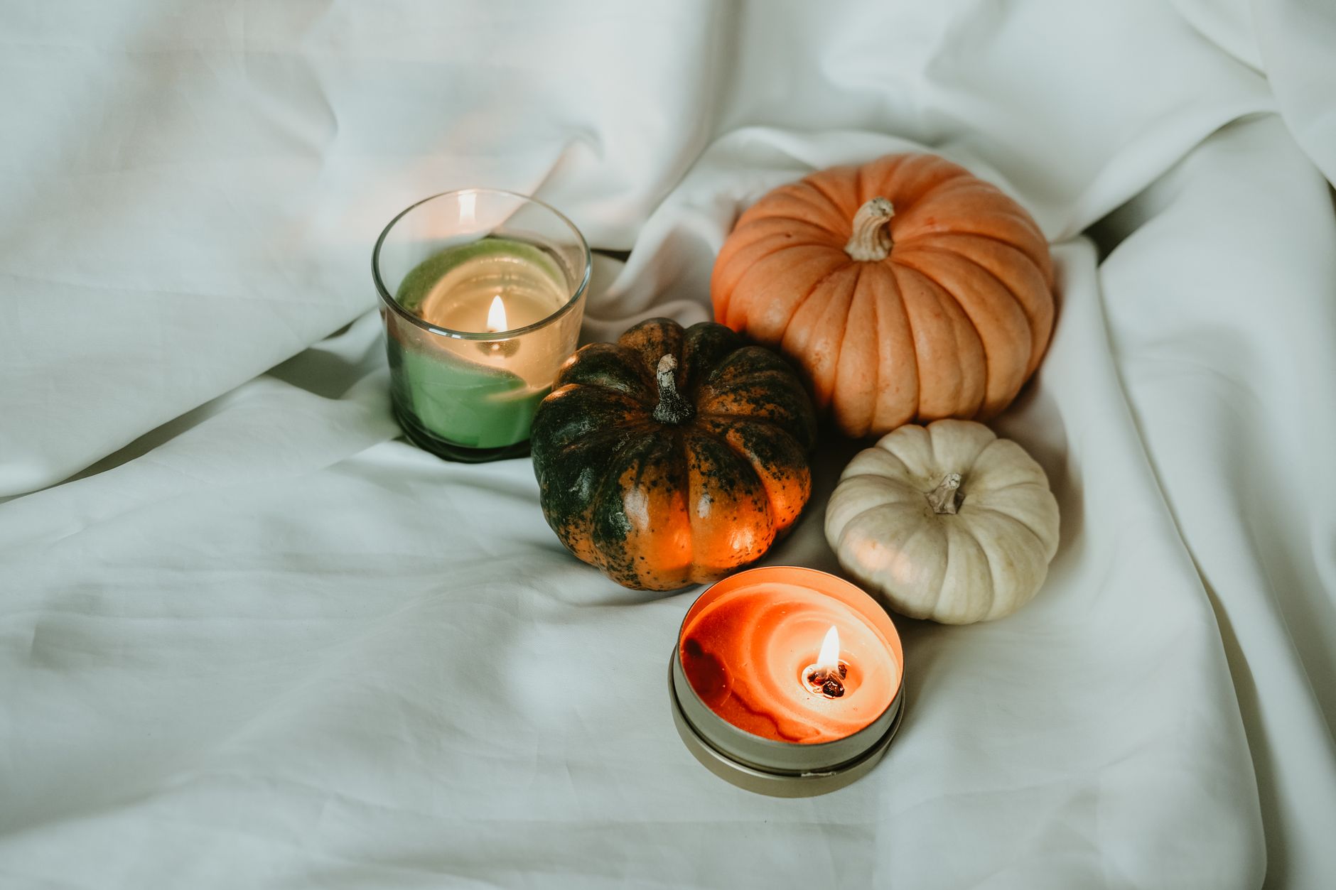 Warm autumn scene featuring pumpkins and candles on a soft white backdrop, perfect for seasonal decor.