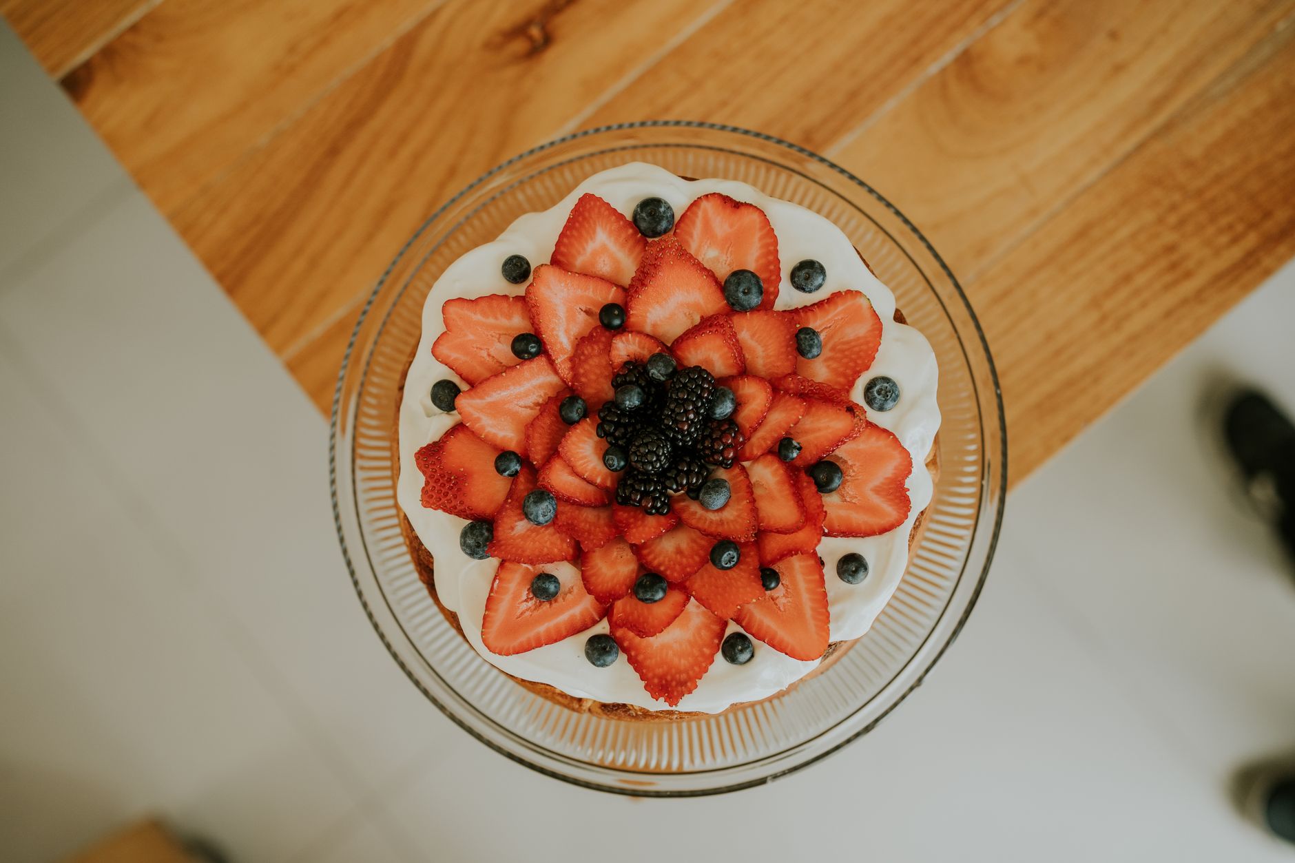 Top view of a beautifully decorated cake with strawberries and blueberries on a wooden table.