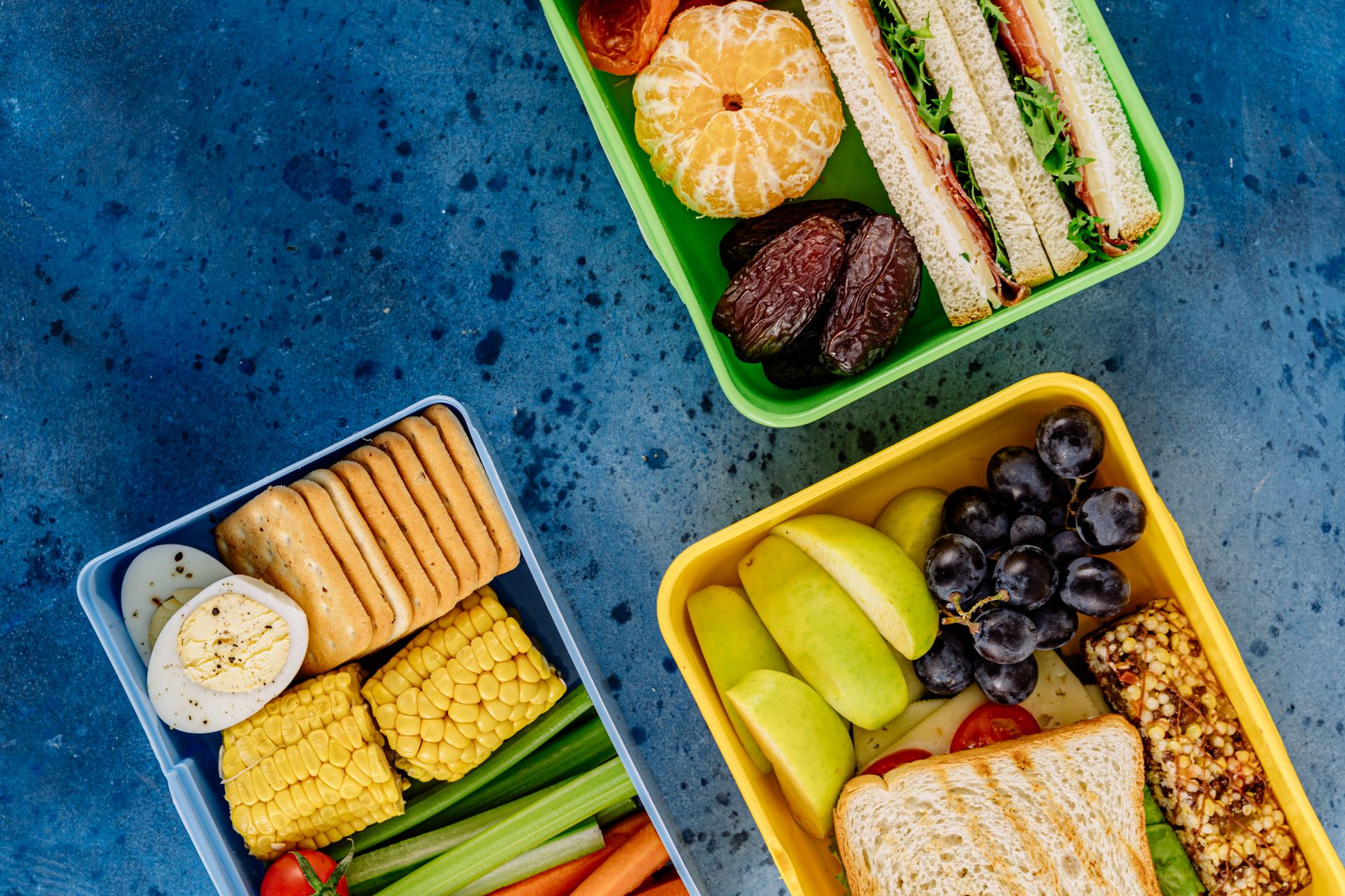 Top view of diverse and healthy lunchbox meals including fruits, veggies, and sandwiches.