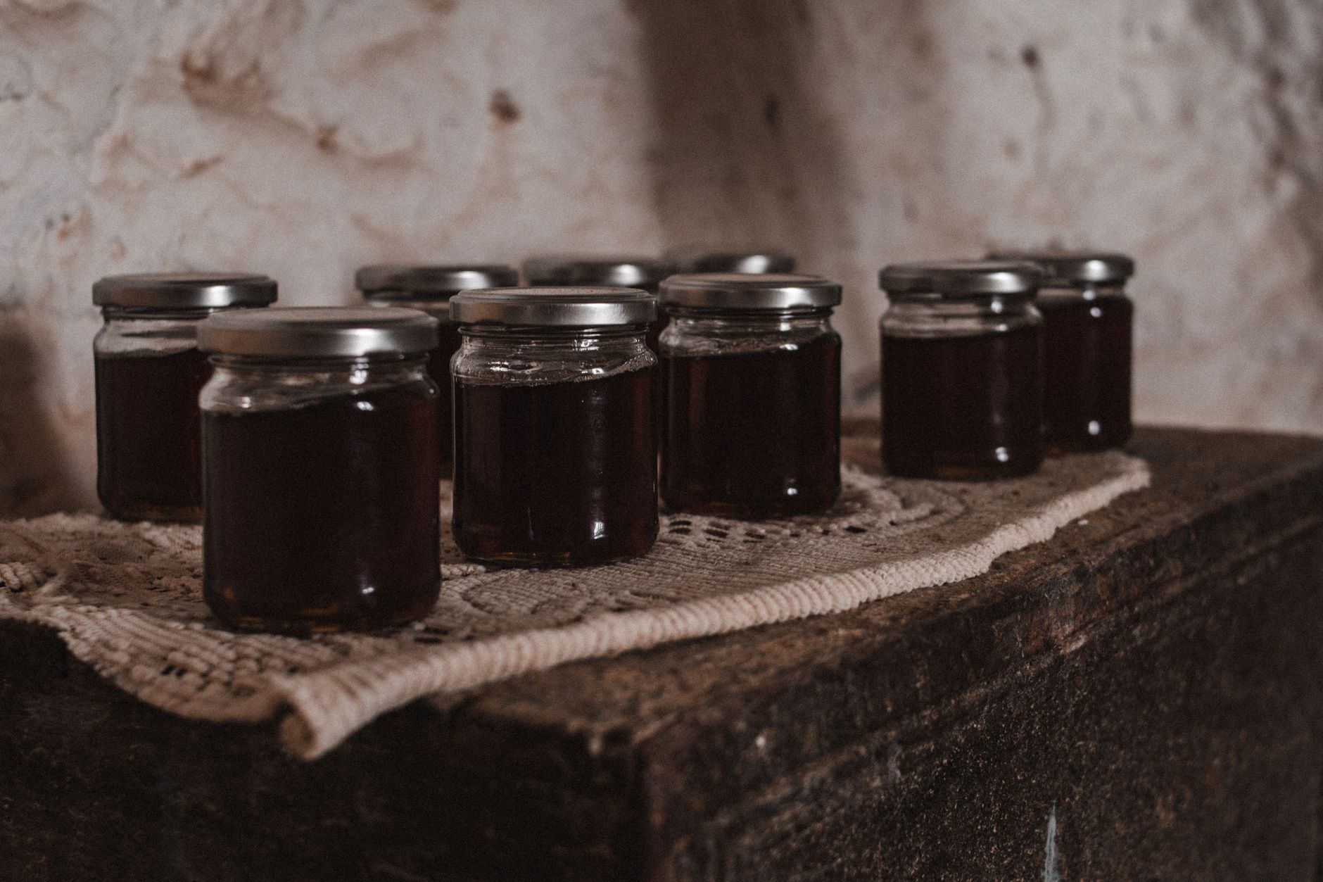 Close-up of glass jars filled with dark homemade preserves displayed on a vintage wooden surface.