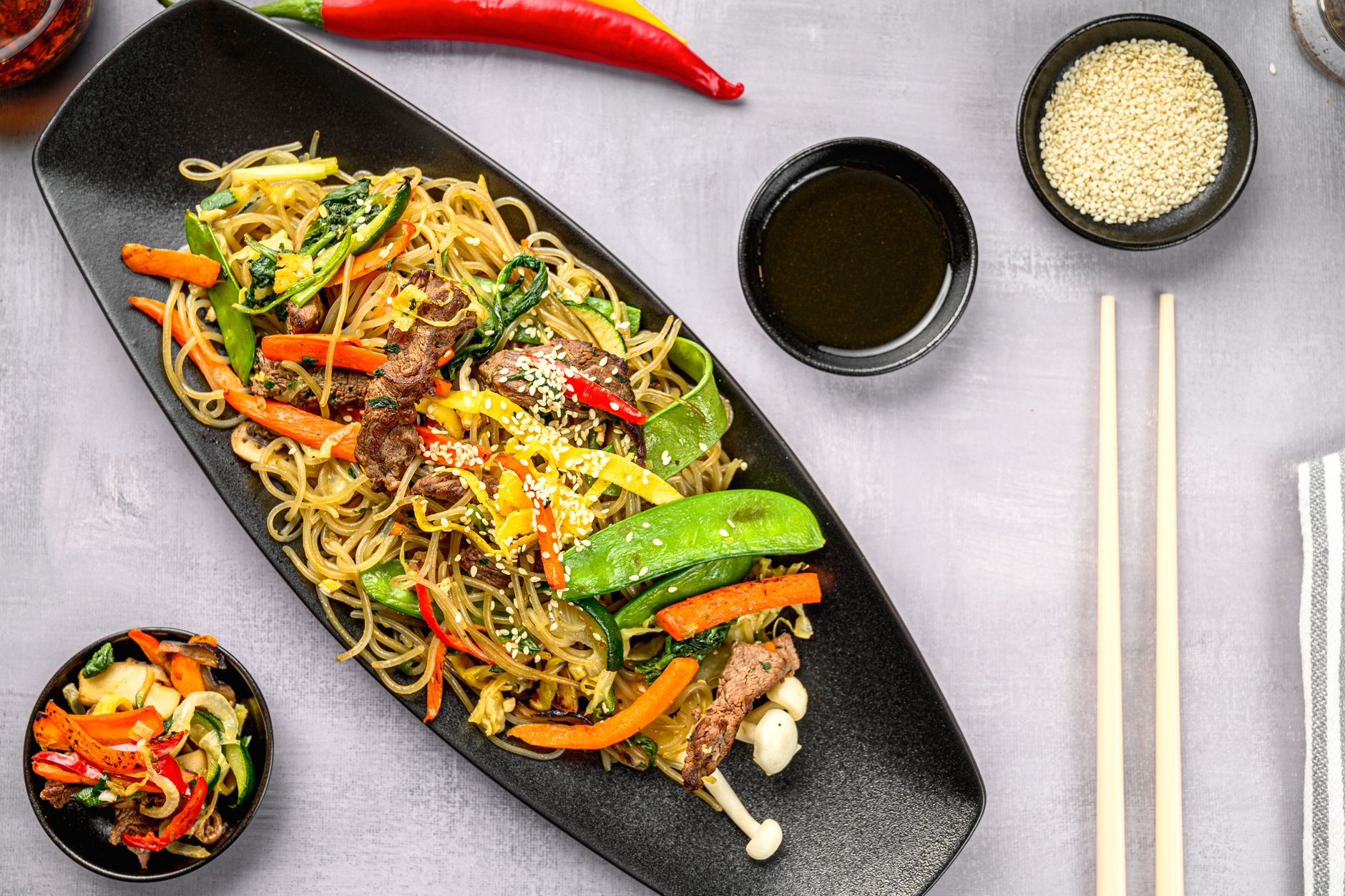 Delicious stir-fry noodles with colorful vegetables and sesame seeds on a black plate.