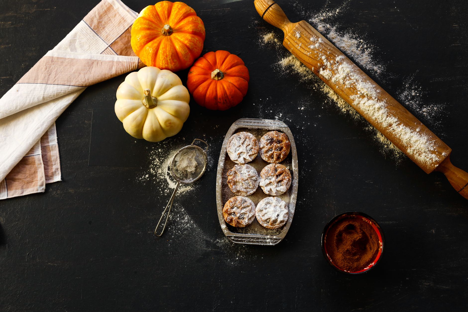 A cozy autumn baking setup with pumpkins, pastries, and baking tools on a dark surface.