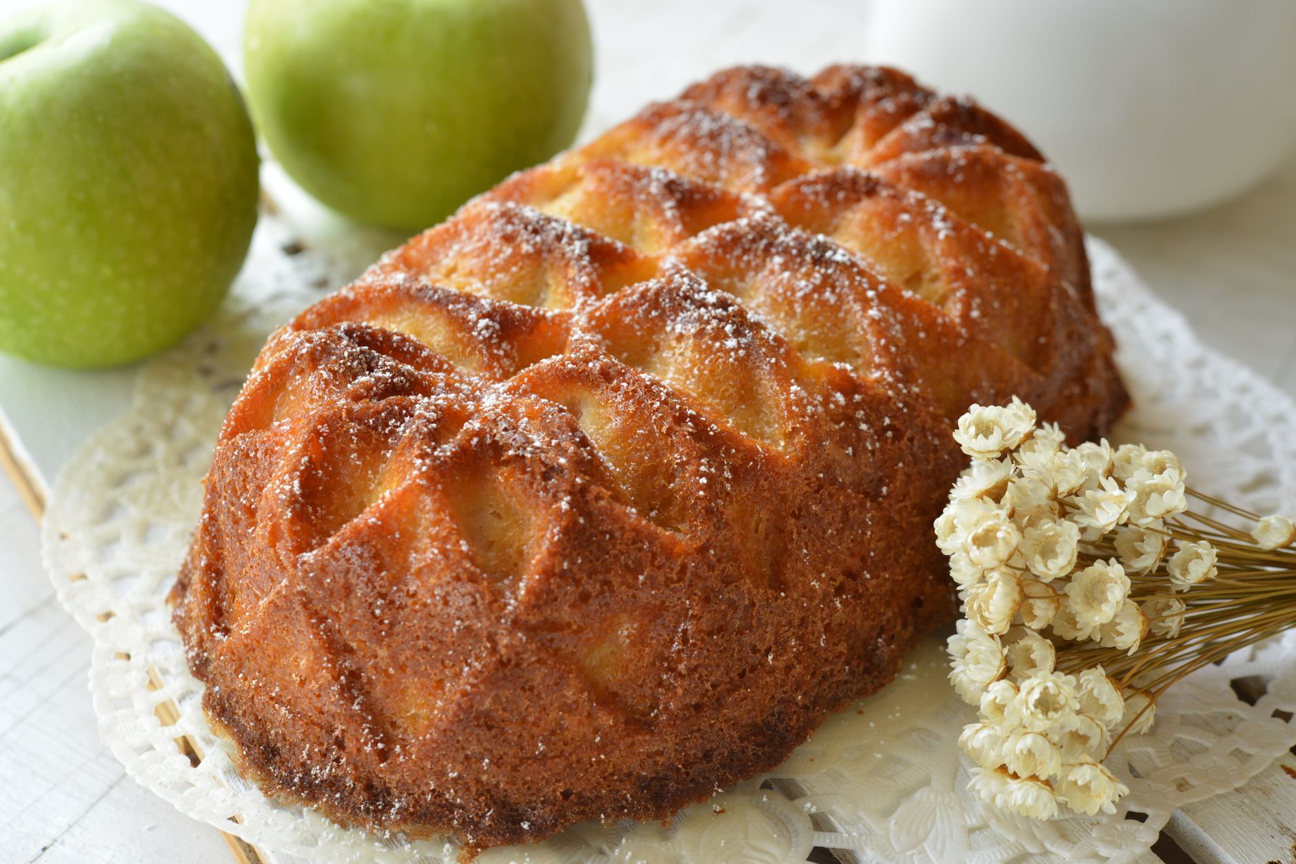Delicious homemade apple cake dusted with sugar, paired with fresh green apples and decorative flowers.