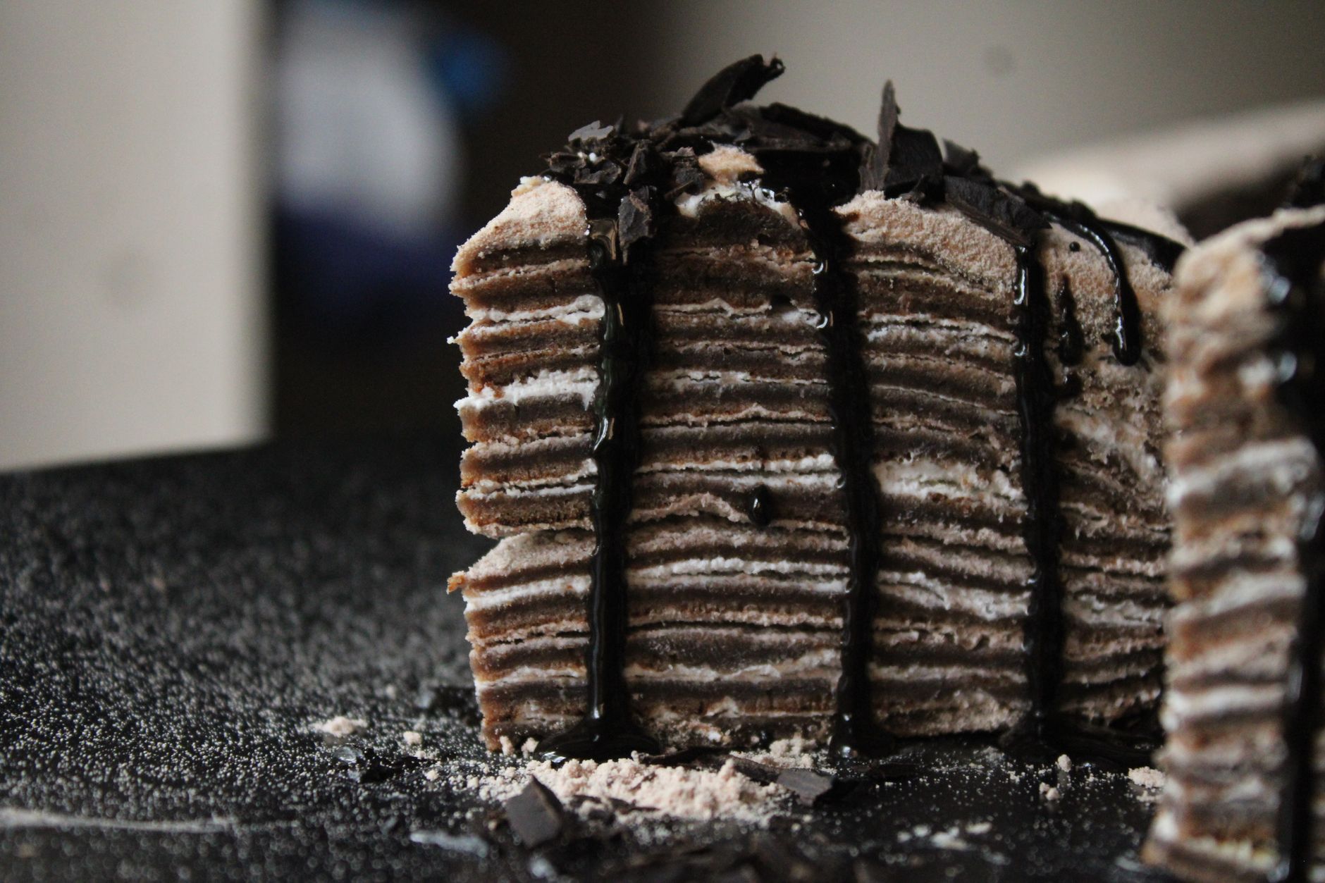 Close-up of a layered chocolate cake topped with dark ganache and sprinkled chocolate shavings.