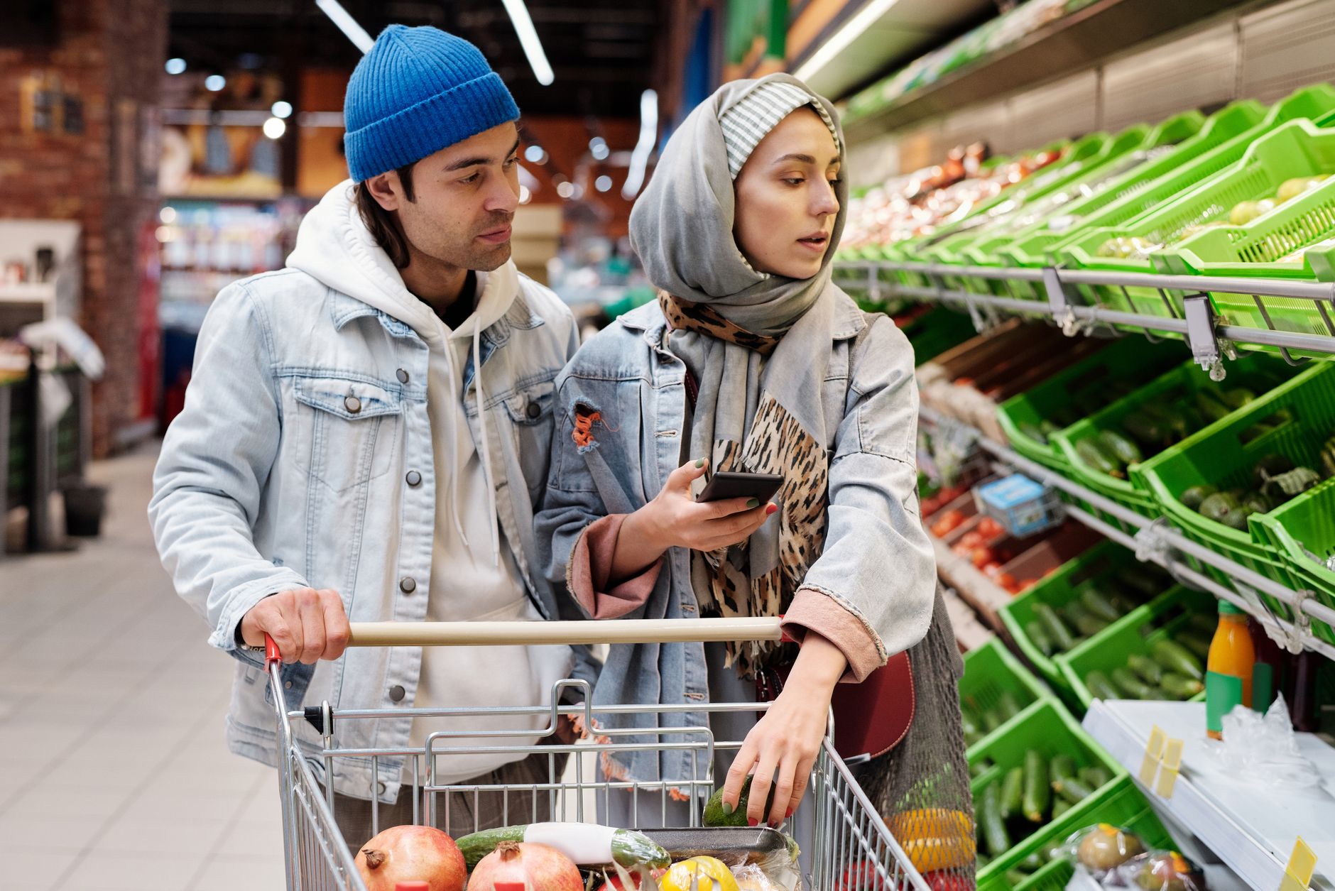 A couple shopping for vegetables in a supermarket, using a smartphone to check their list.