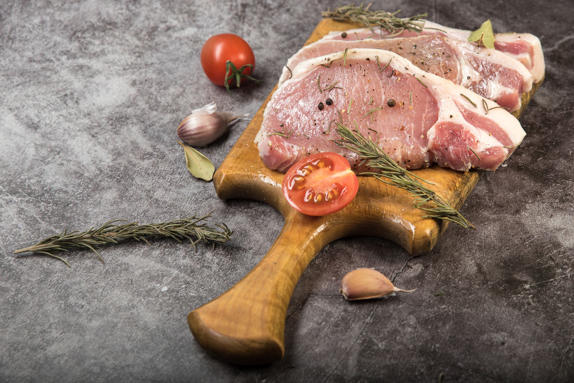 Fresh raw pork chops with rosemary and peppercorns, ready for cooking.