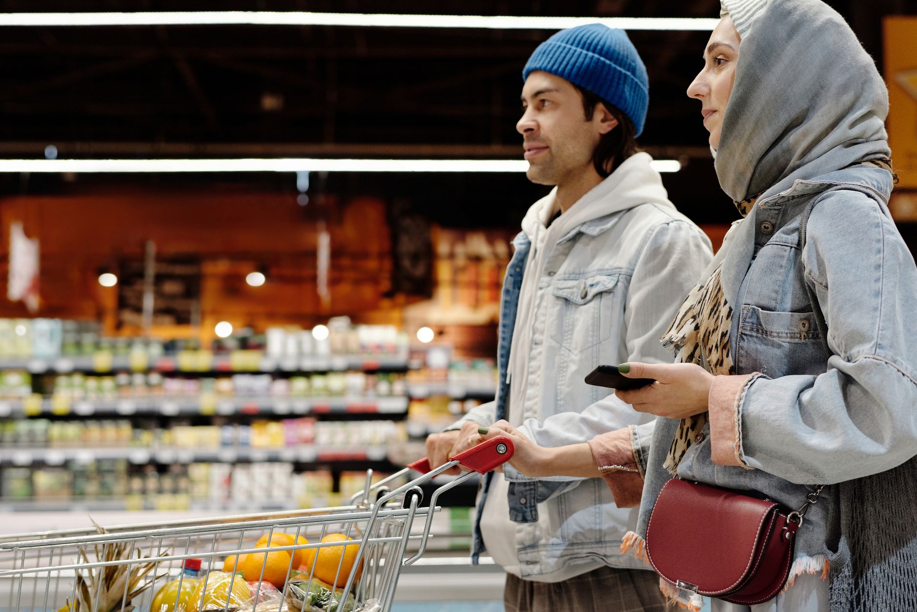 A young couple shopping with a cart in a supermarket aisle, selecting fresh produce.