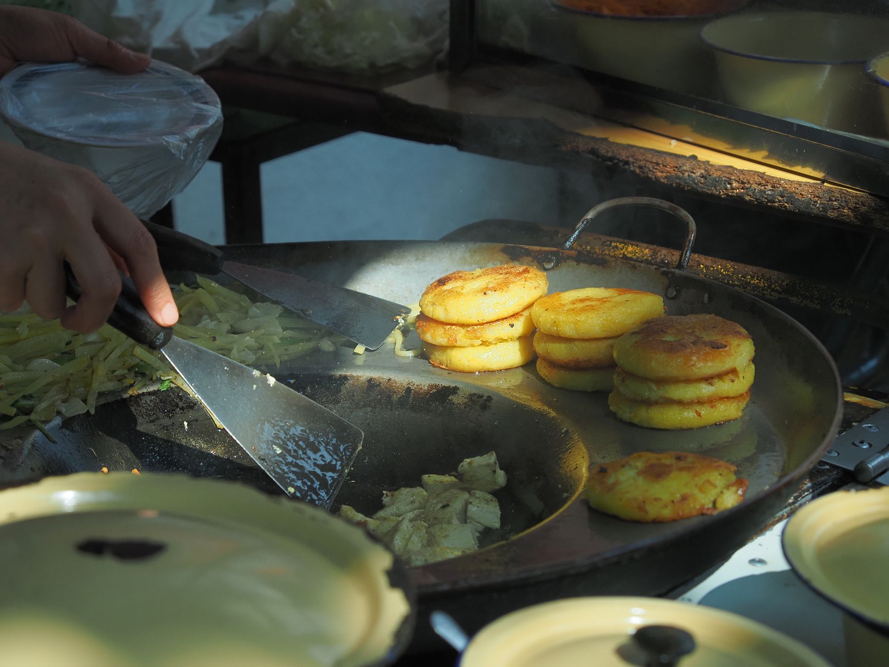 Street food vendor cooking potato patties on a large frying pan outdoors.
